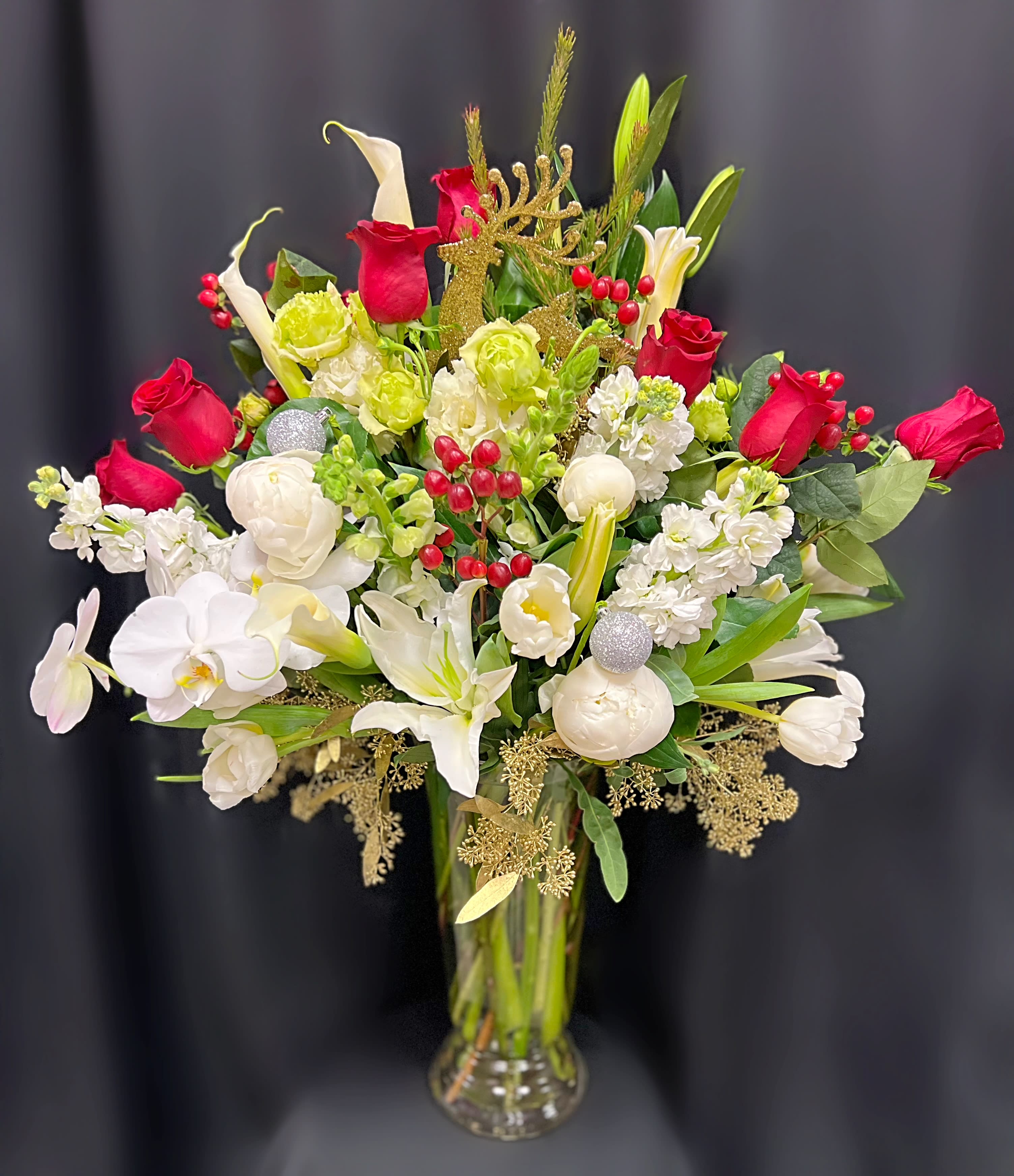 Red and white floral arrangement in a clear glass vase with gold holiday accents