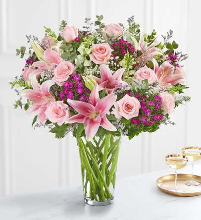 Pink lilies and roses arranged in a clear glass vase