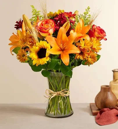 Bouquet of orange lilies, roses, and sunflowers in a glass vase
