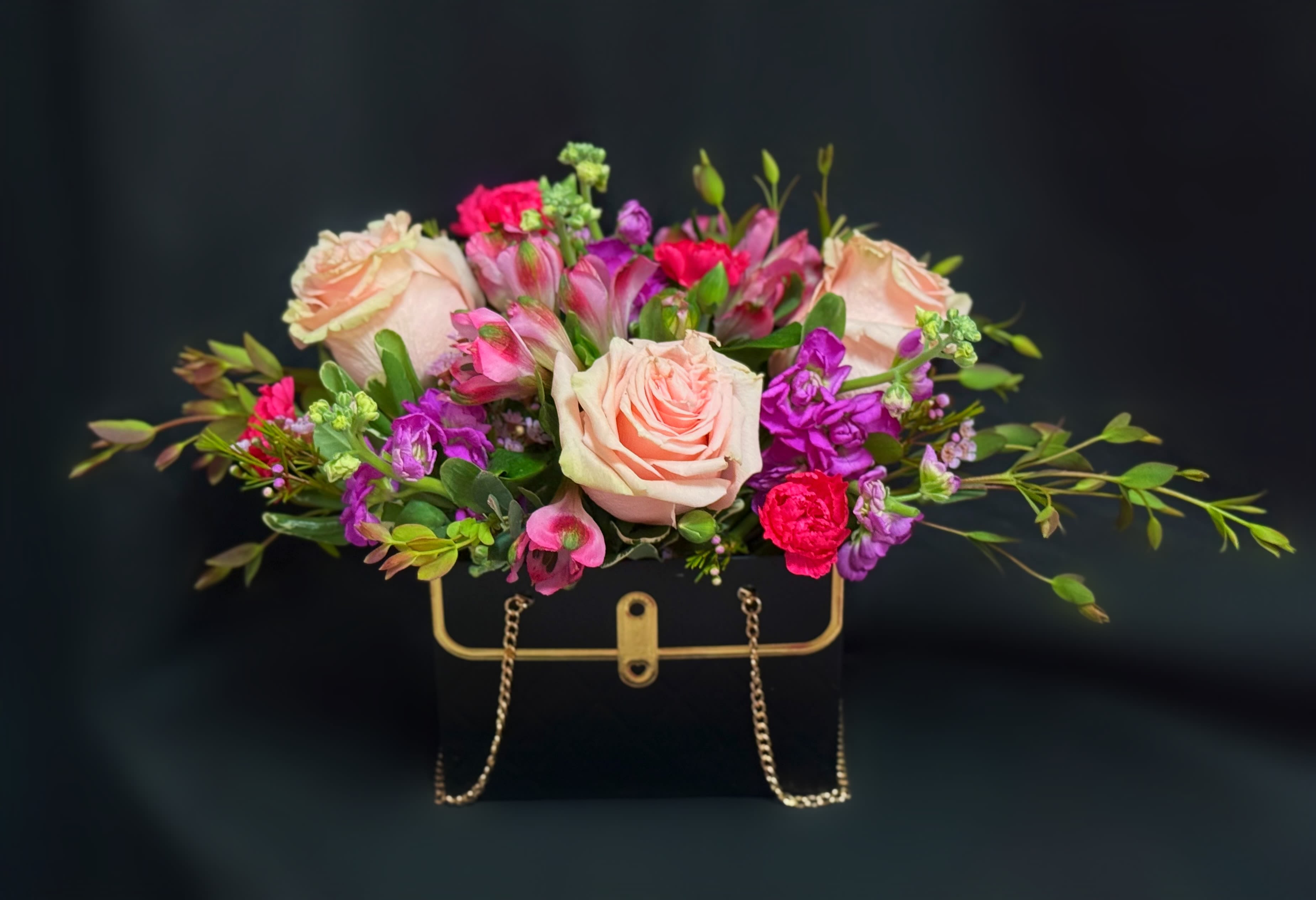 Pink and purple flower arrangement in a black handbag-shaped container