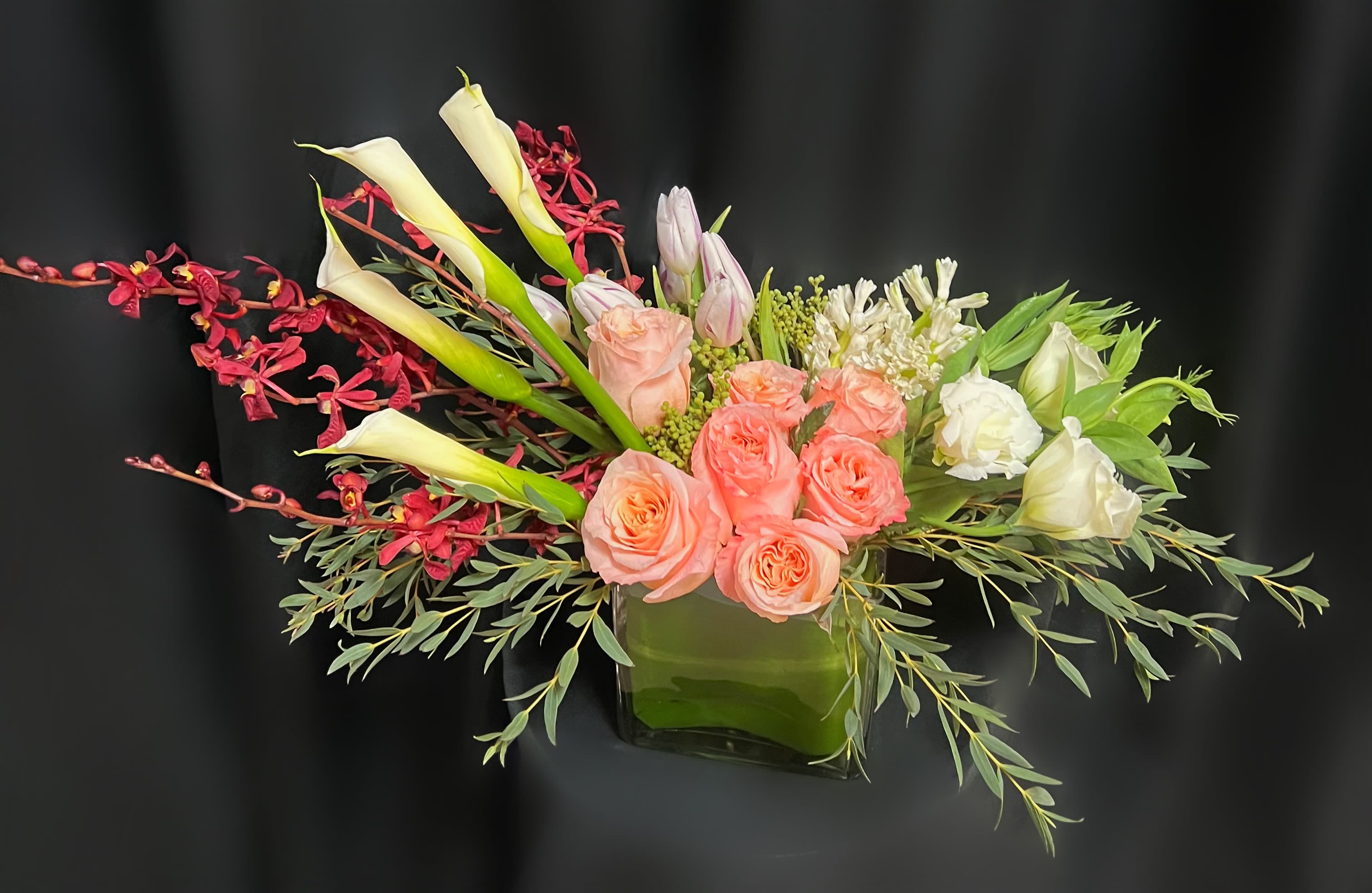 Pink roses and white calla lilies in a glass vase with red orchids
