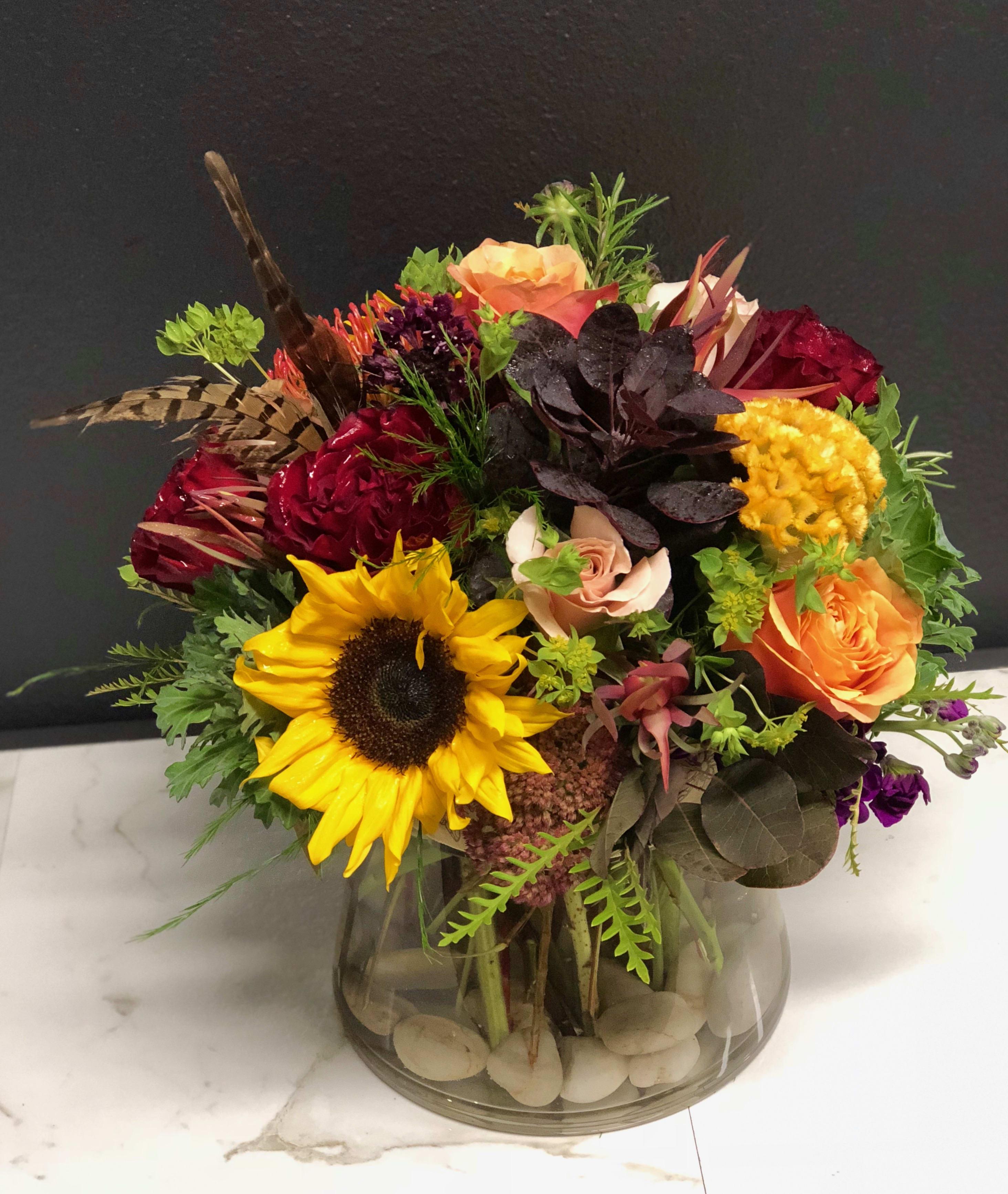 Mixed bouquet in a glass vase with a sunflower, roses, and bright accent flowers