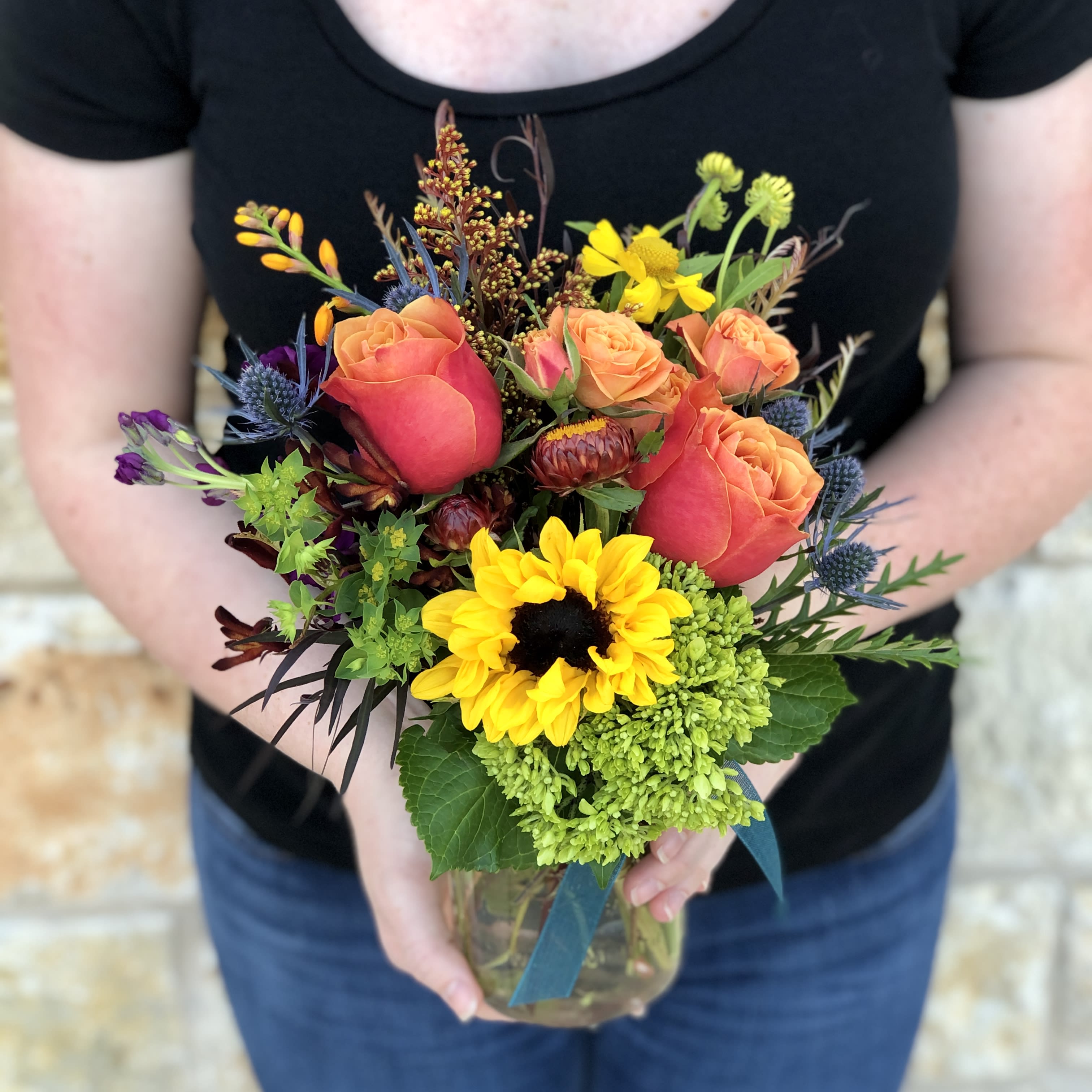 Mixed bouquet of orange roses, sunflowers, and green hydrangea in a glass vase