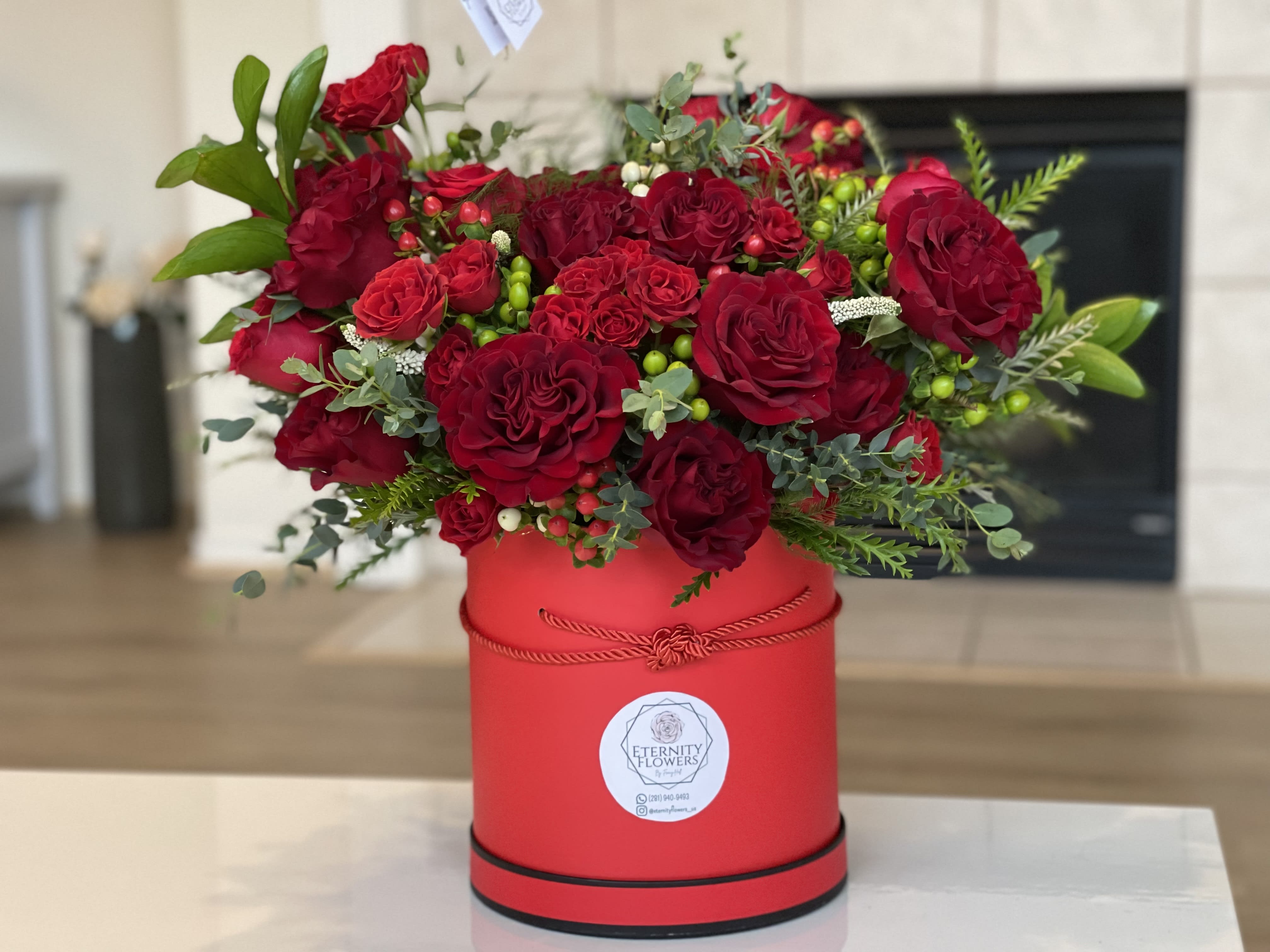 Red roses arranged in a red round box with greenery