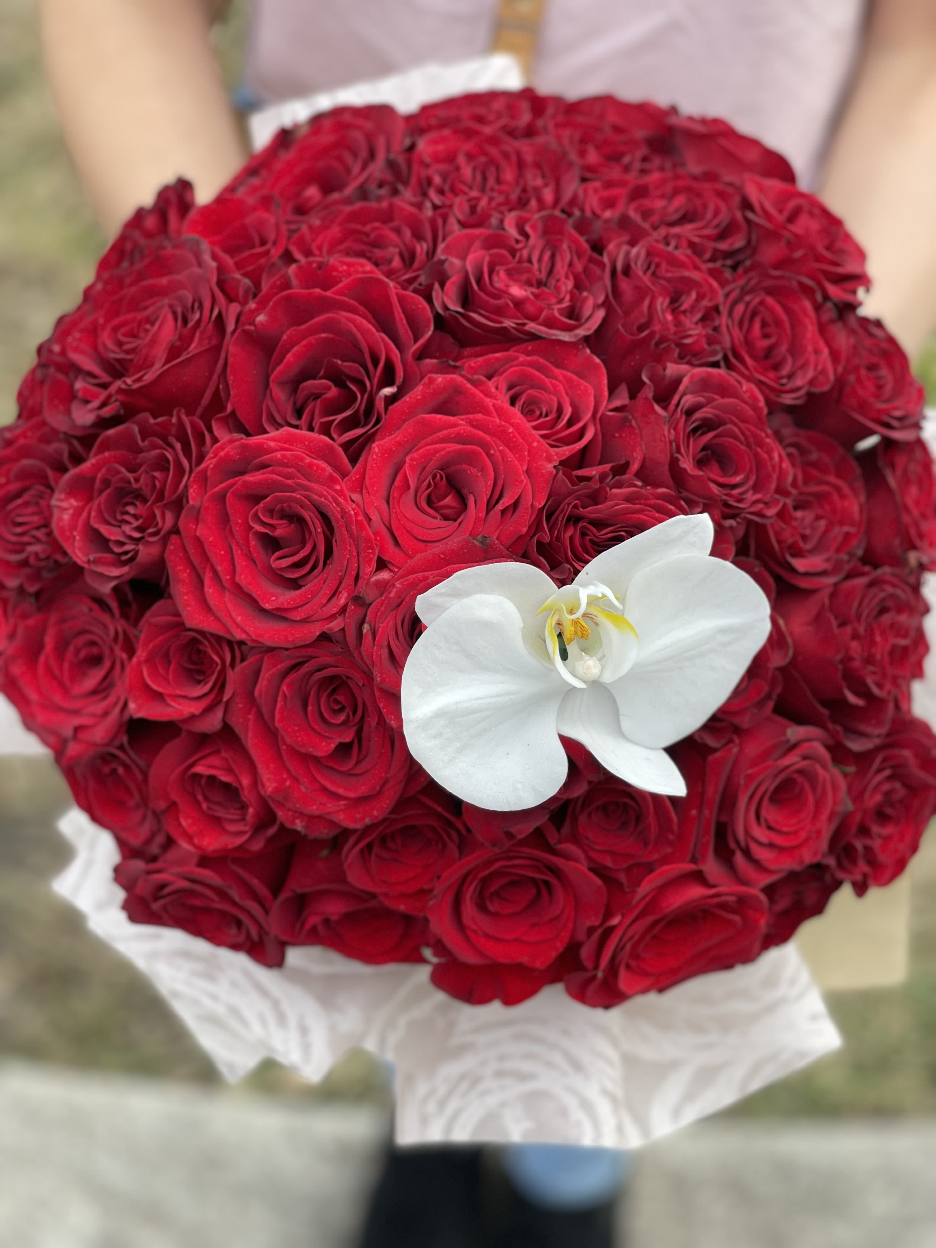 Round bouquet of red roses with a white orchid accent