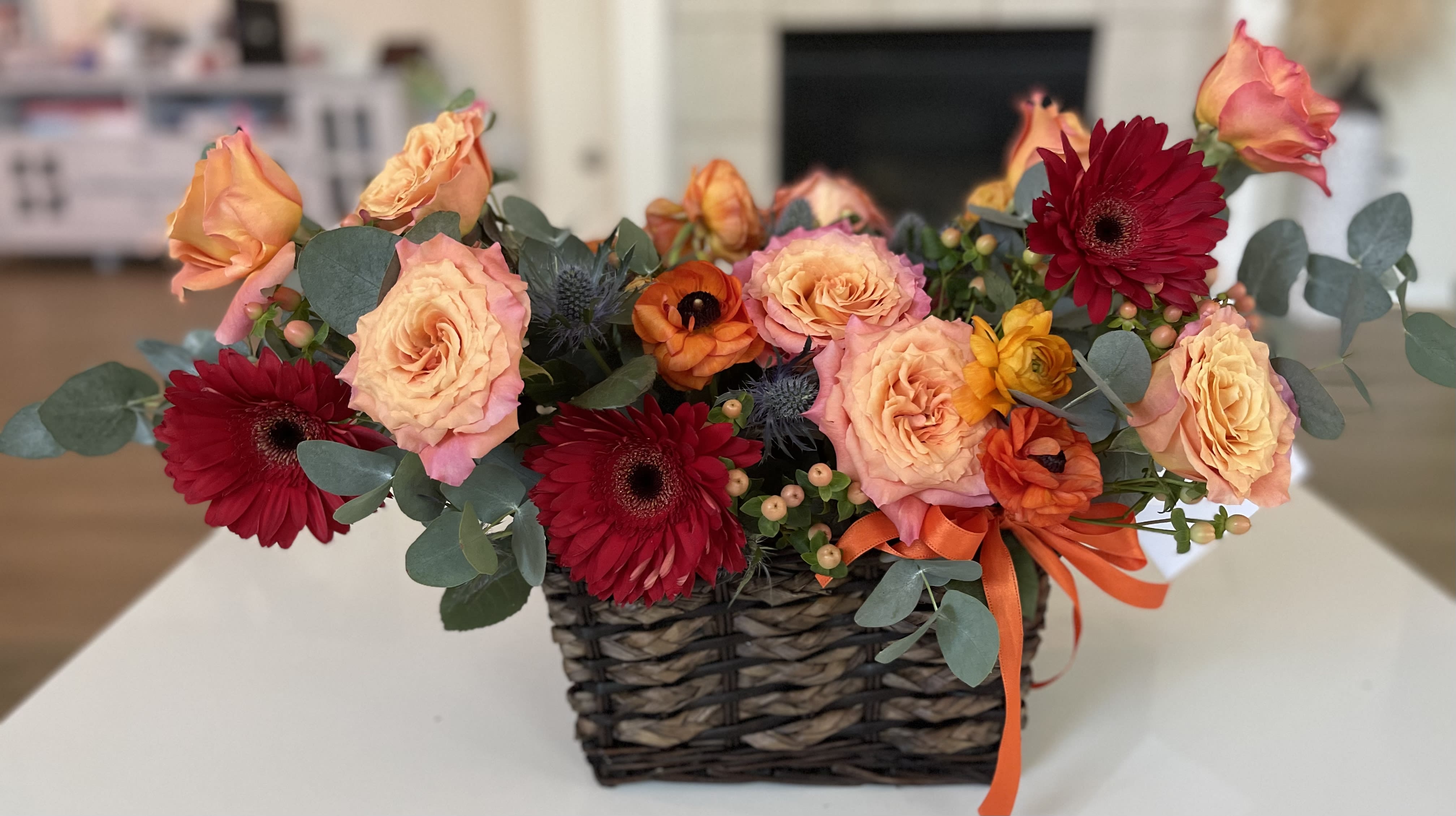 Basket arrangement of peach roses and red gerbera daisies