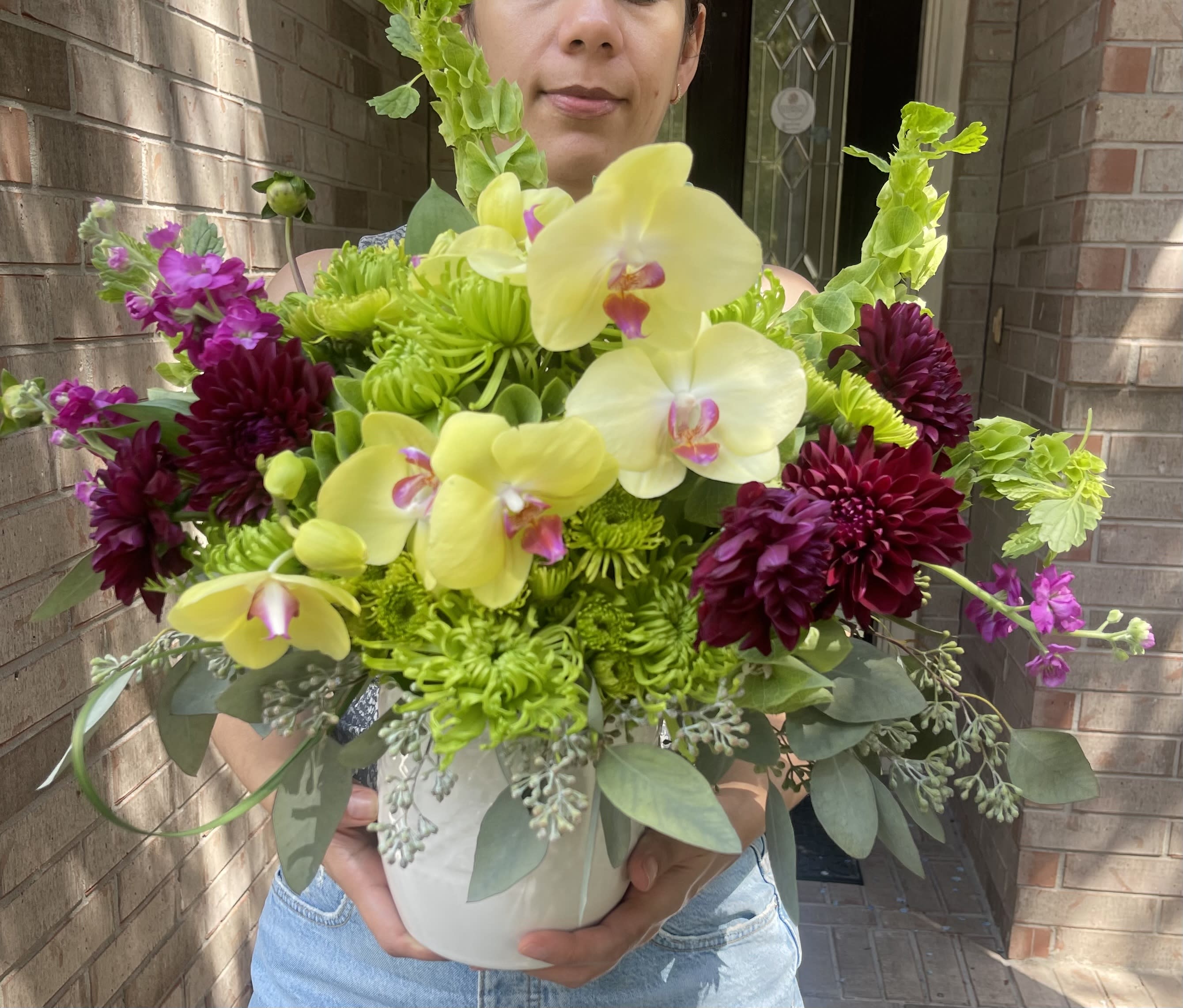 Bouquet of yellow orchids and dark purple flowers in a white vase