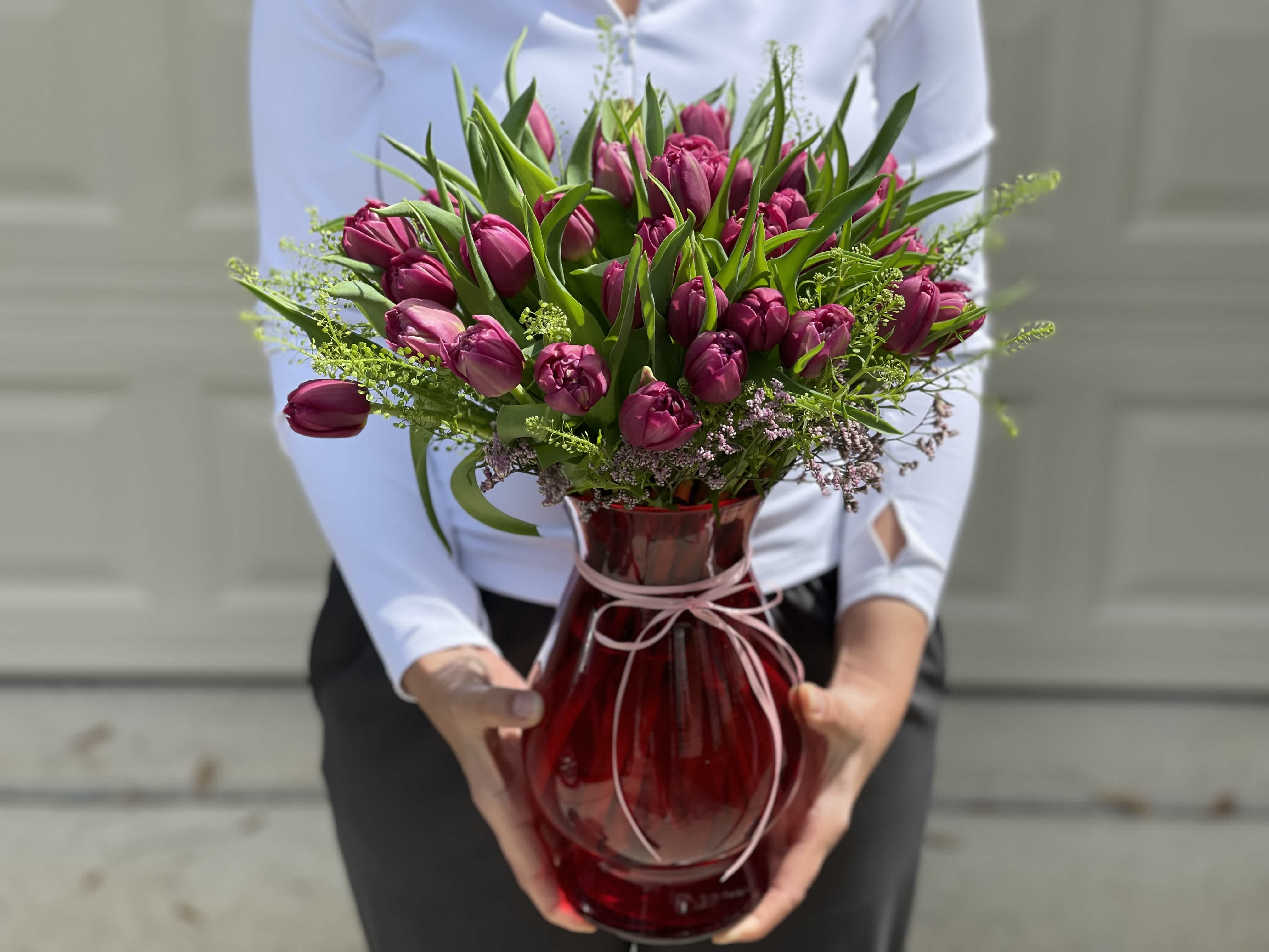 Magenta tulip bouquet in a red glass vase with a pink ribbon