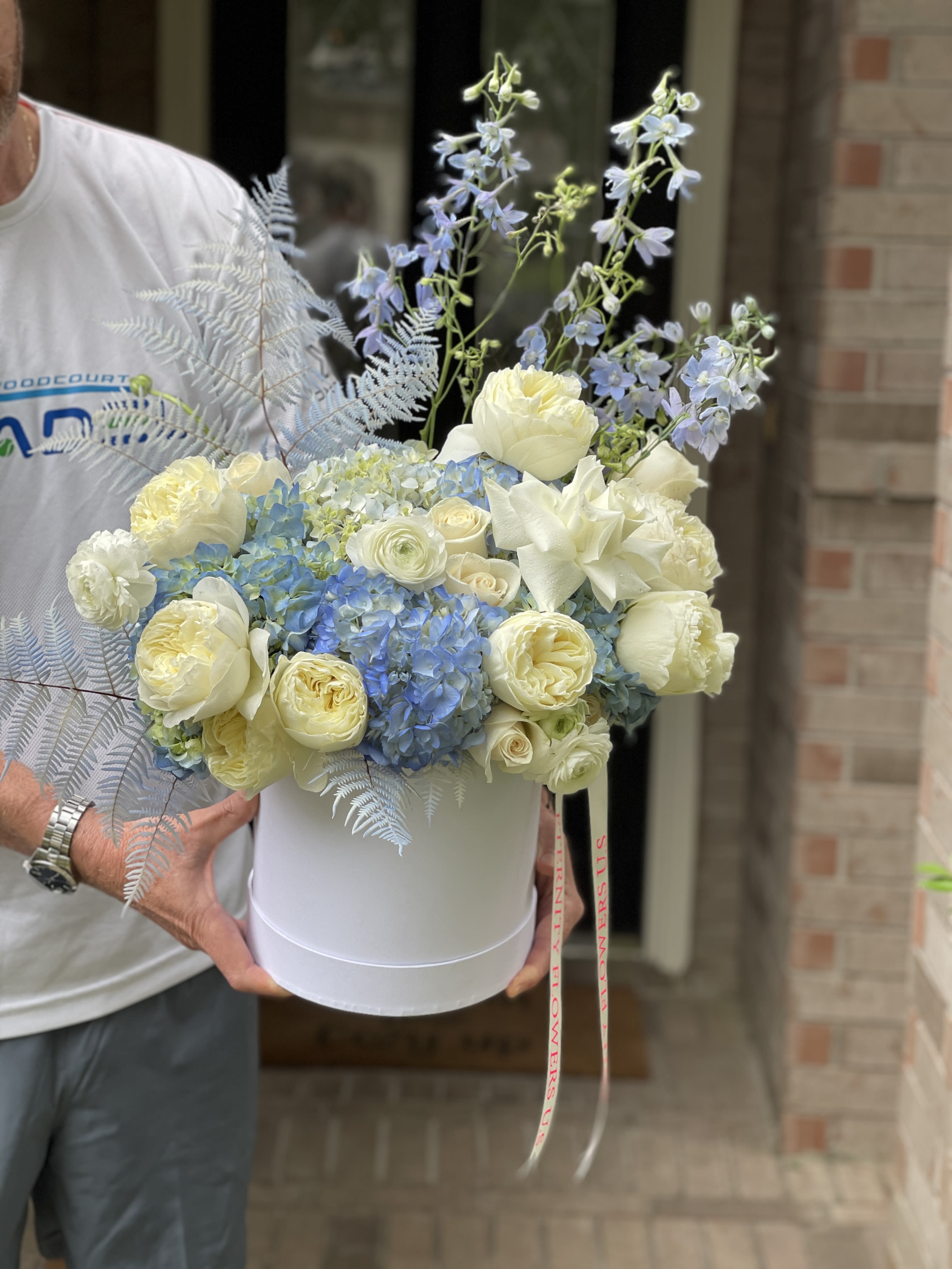 White hatbox arrangement with cream roses, blue hydrangeas, and pale blue delphinium