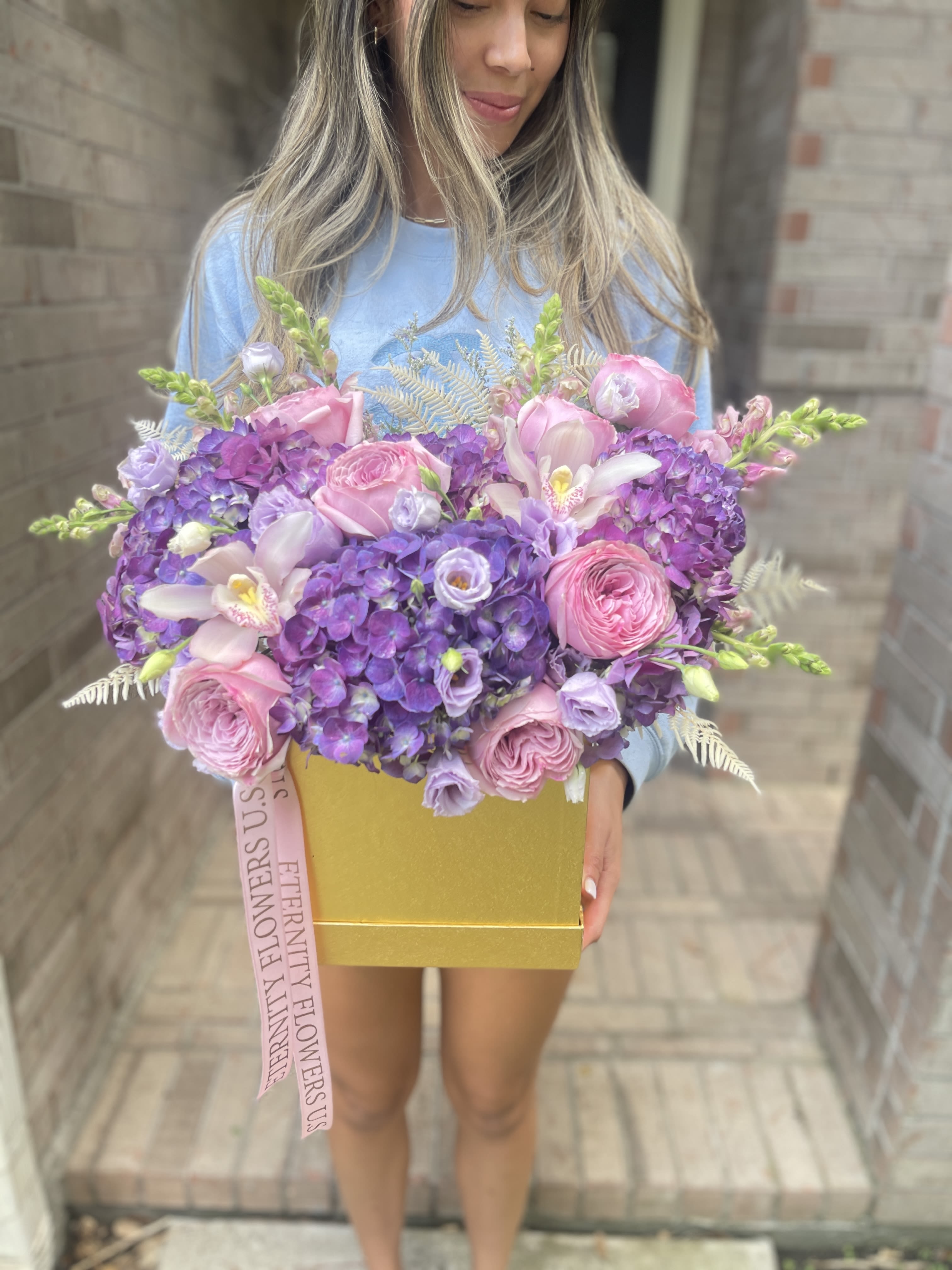 Large pink and purple flower arrangement in a gold box