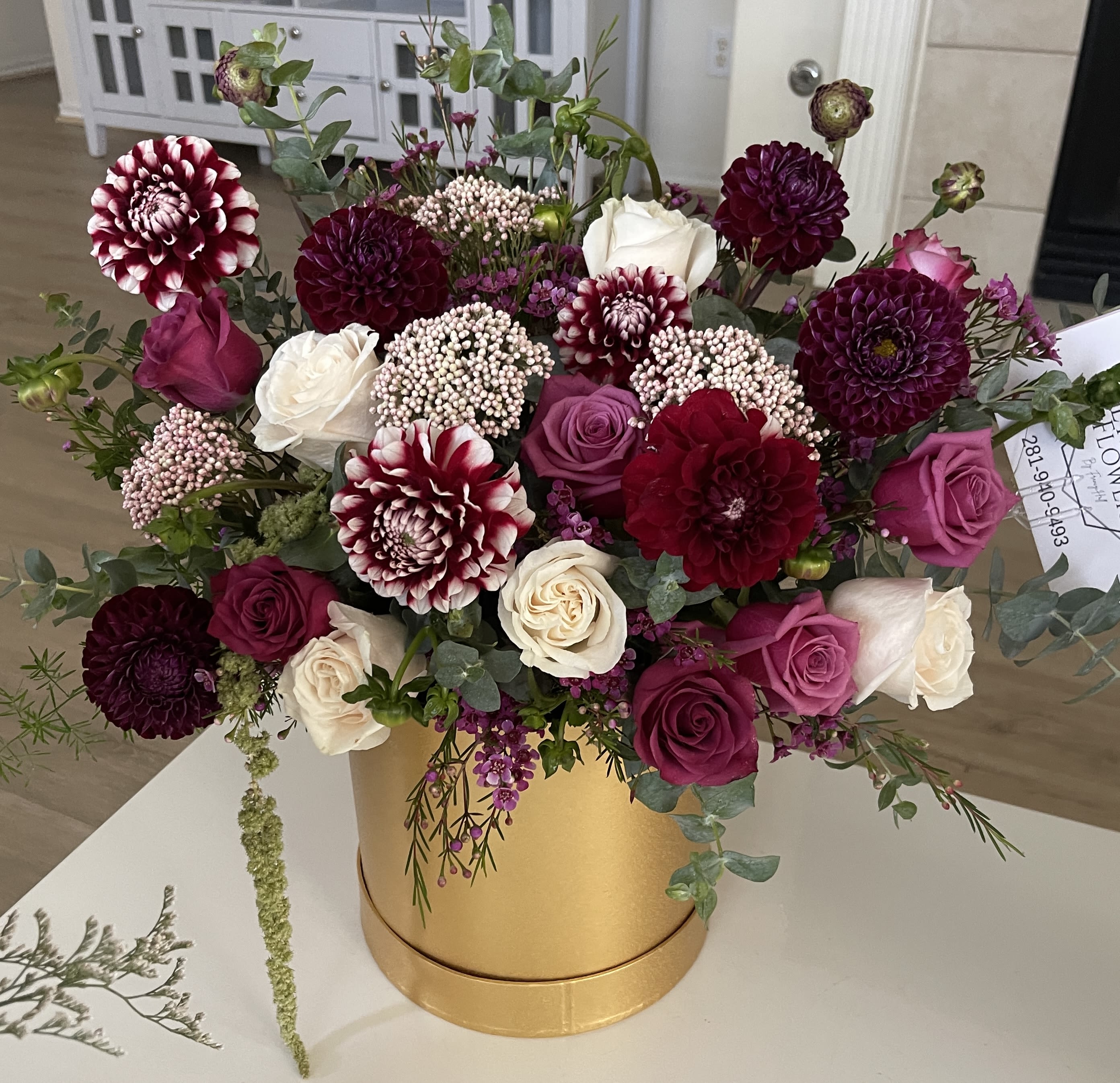 Burgundy dahlias and pink and cream roses arranged in a gold cylinder box.