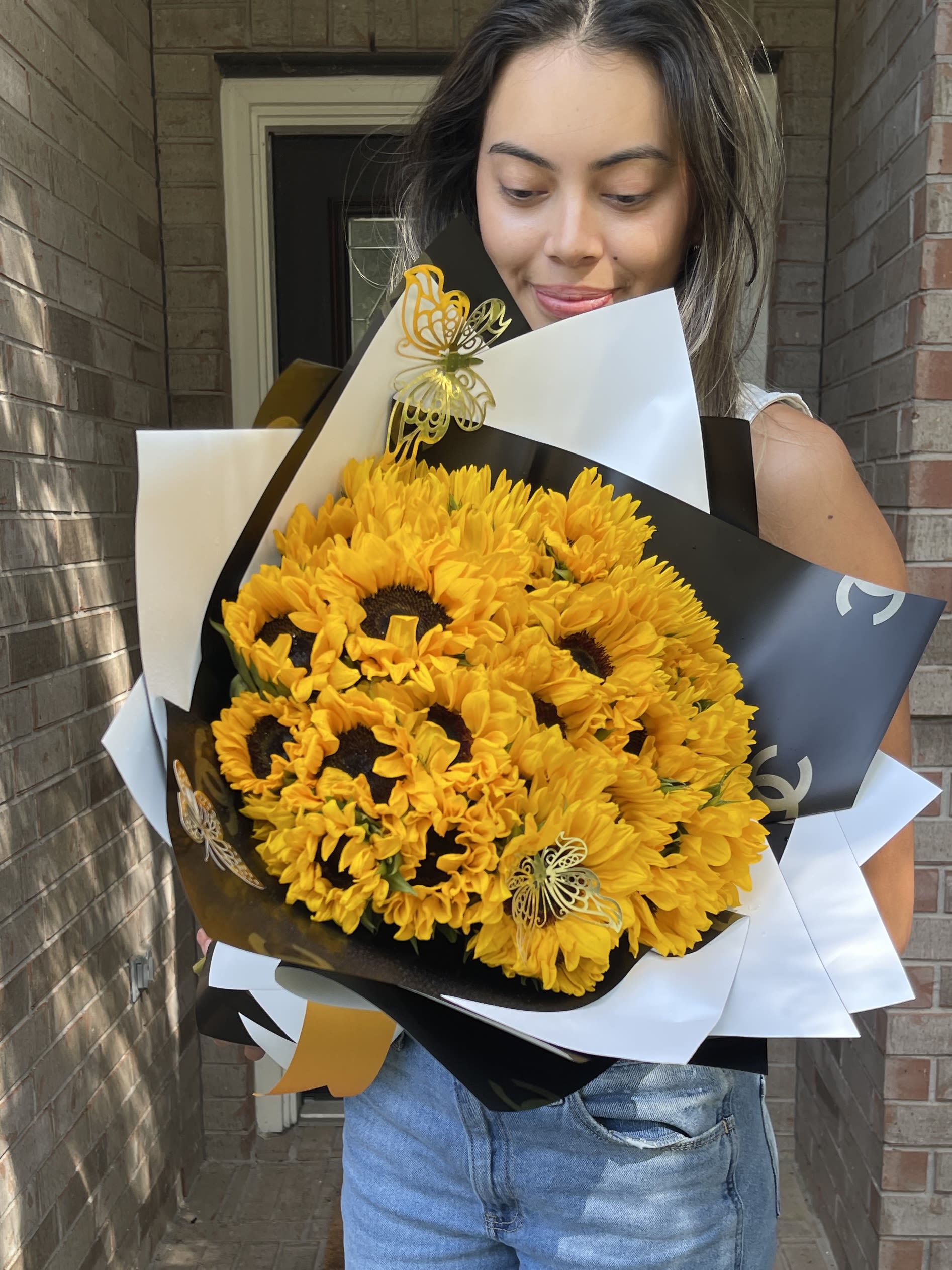 Woman holding a large bouquet of yellow sunflowers wrapped in black and white paper