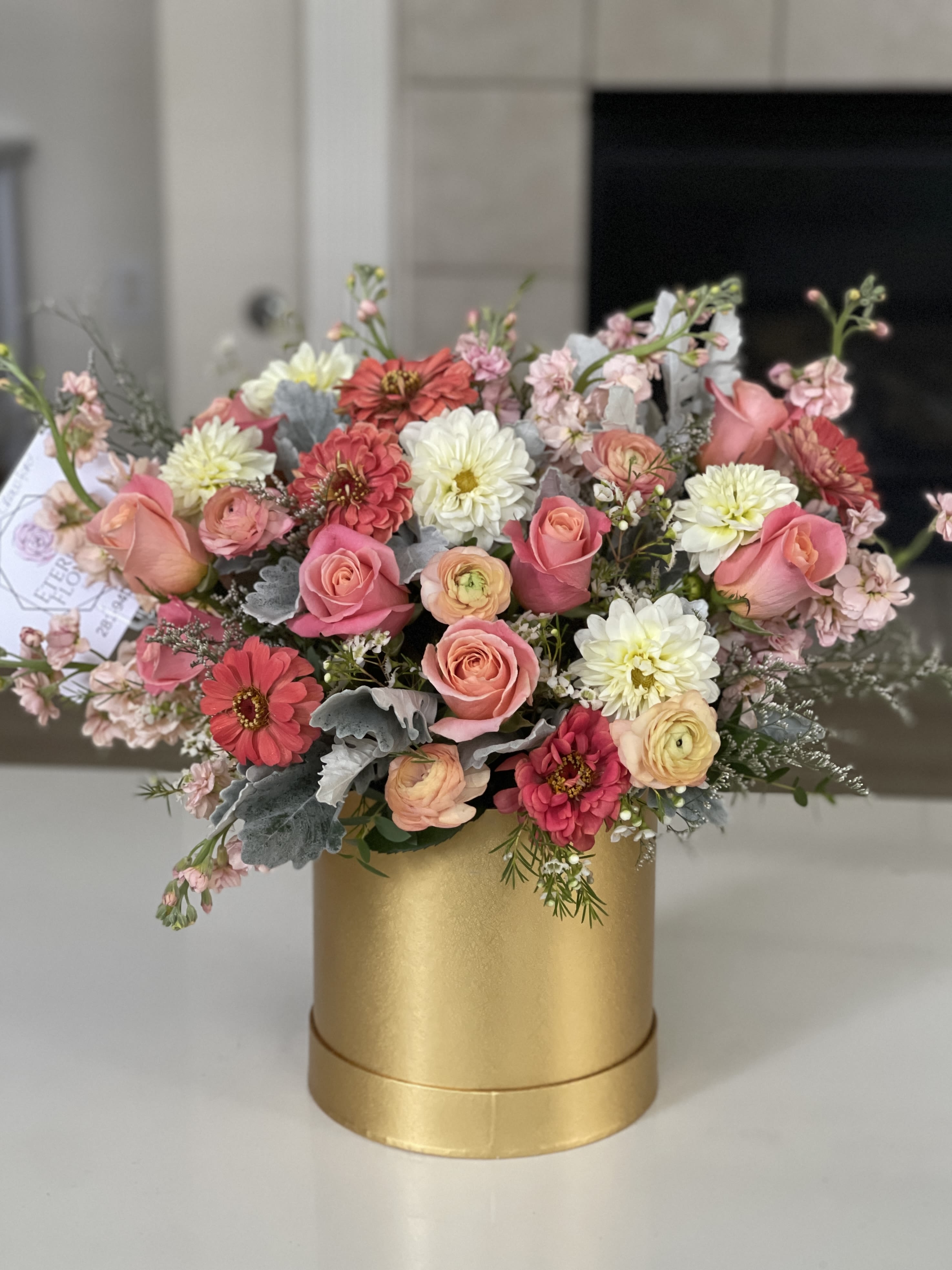 Pink and white mixed flowers arranged in a gold cylindrical box