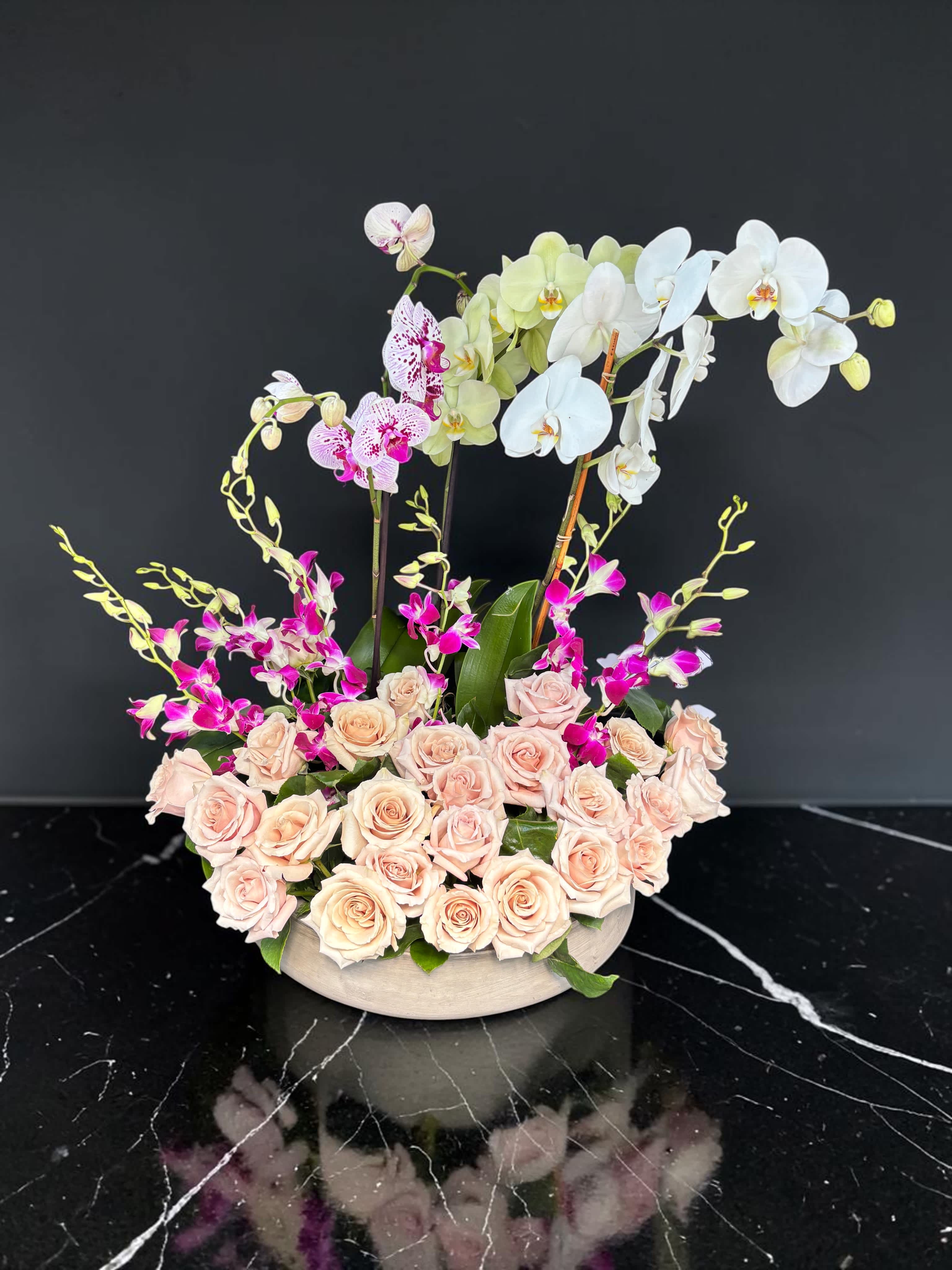 Arrangement of pale roses and orchids in a low round container