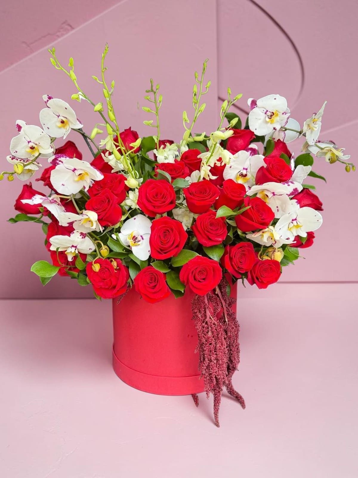 Red roses and white orchids arranged in a pink hat box