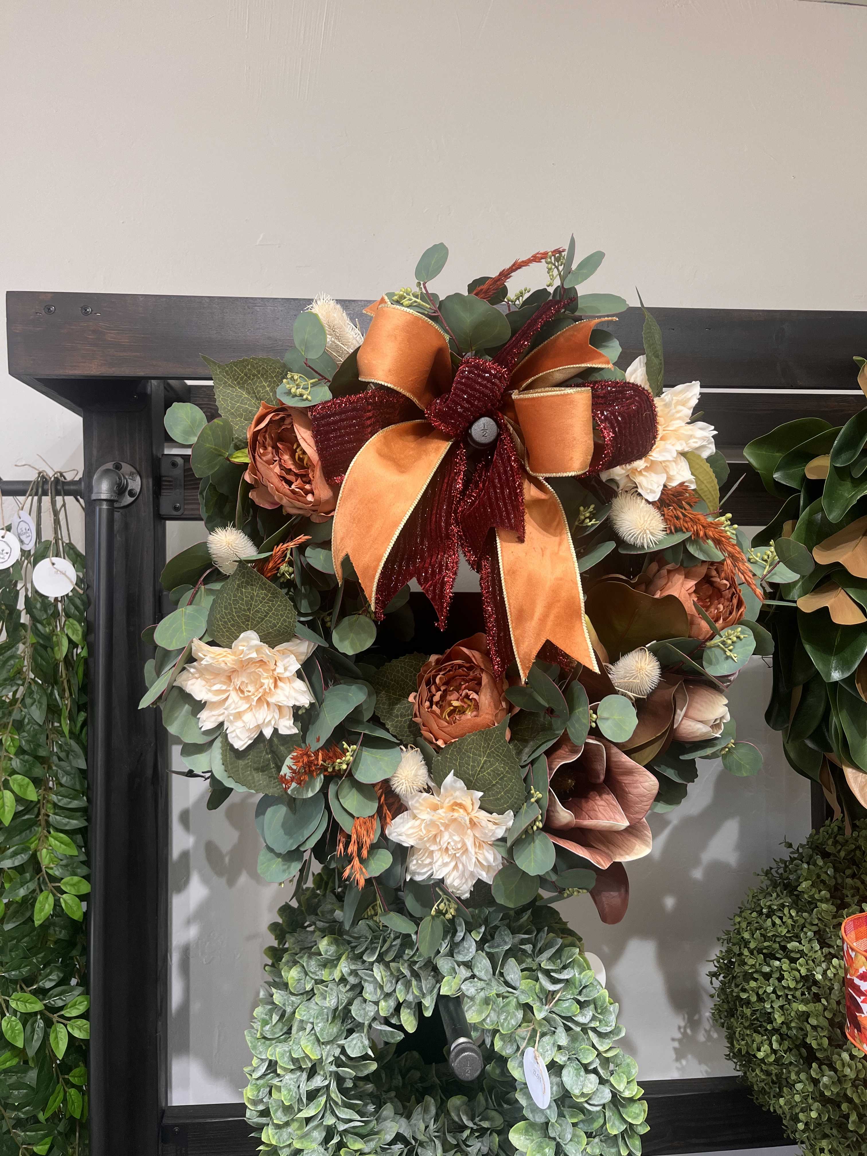 Fall wreath with orange ribbon, cream flowers, and eucalyptus on a dark frame