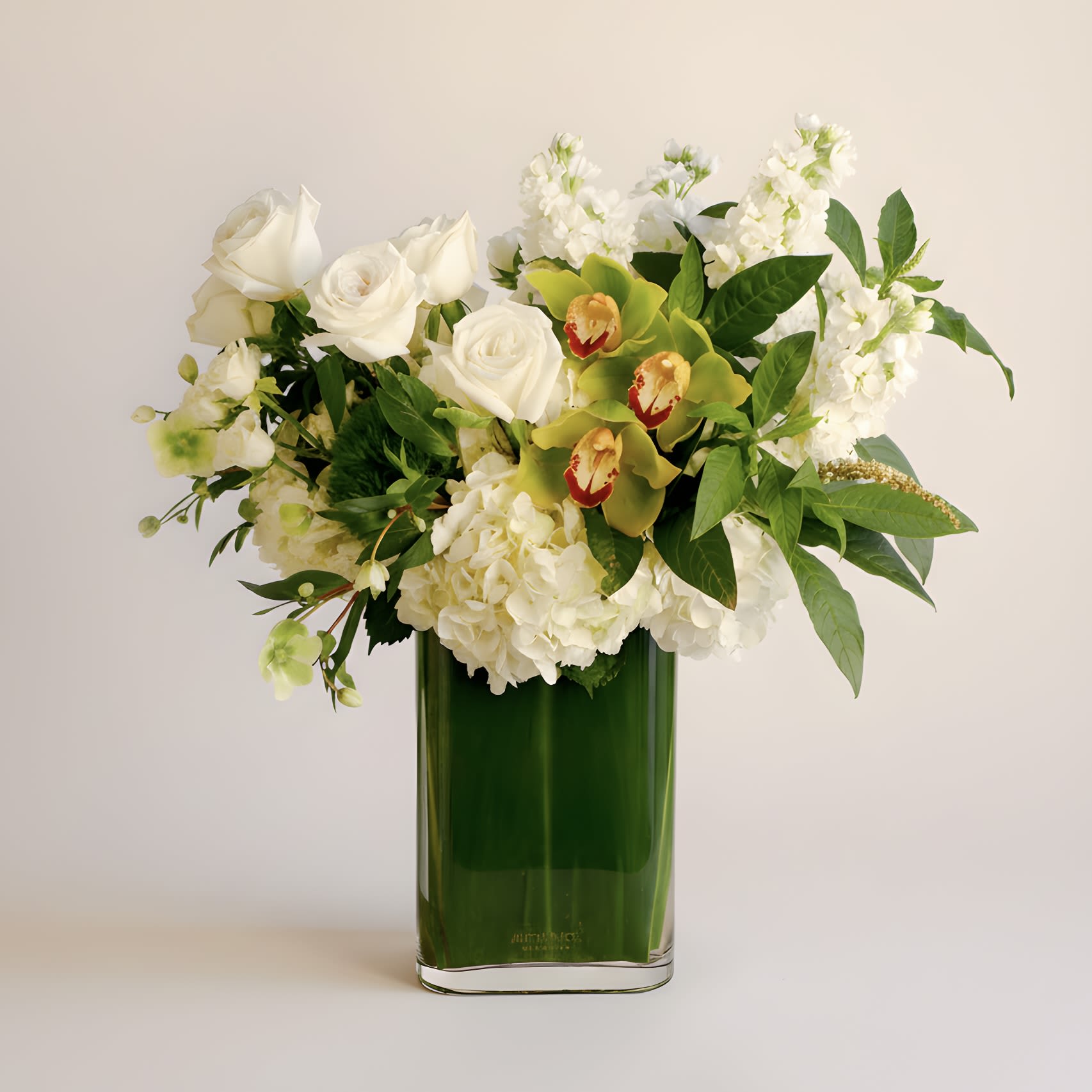 Emerald Elegance - This modern arrangement features an elegant collection of green cymbidium orchids, white roses, hydrangeas, hellebores, fragrant stock and more in a tall rectangular leaf-lined glass vase. Approximately measures 20 inches tall and 18 inches wide with flowers.