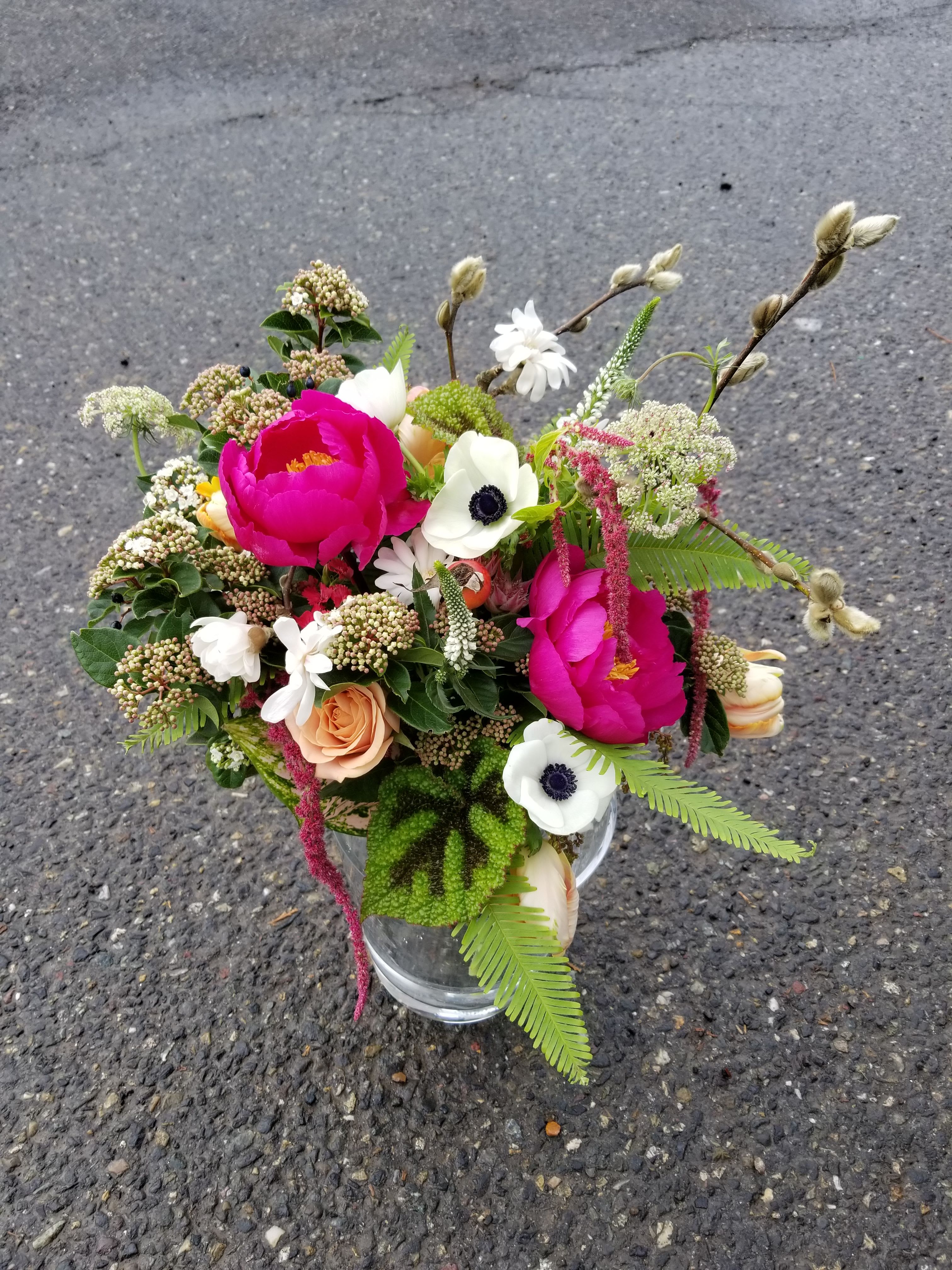 Mixed arrangement of hot pink blooms, white anemones, and peach roses in a clear glass vase