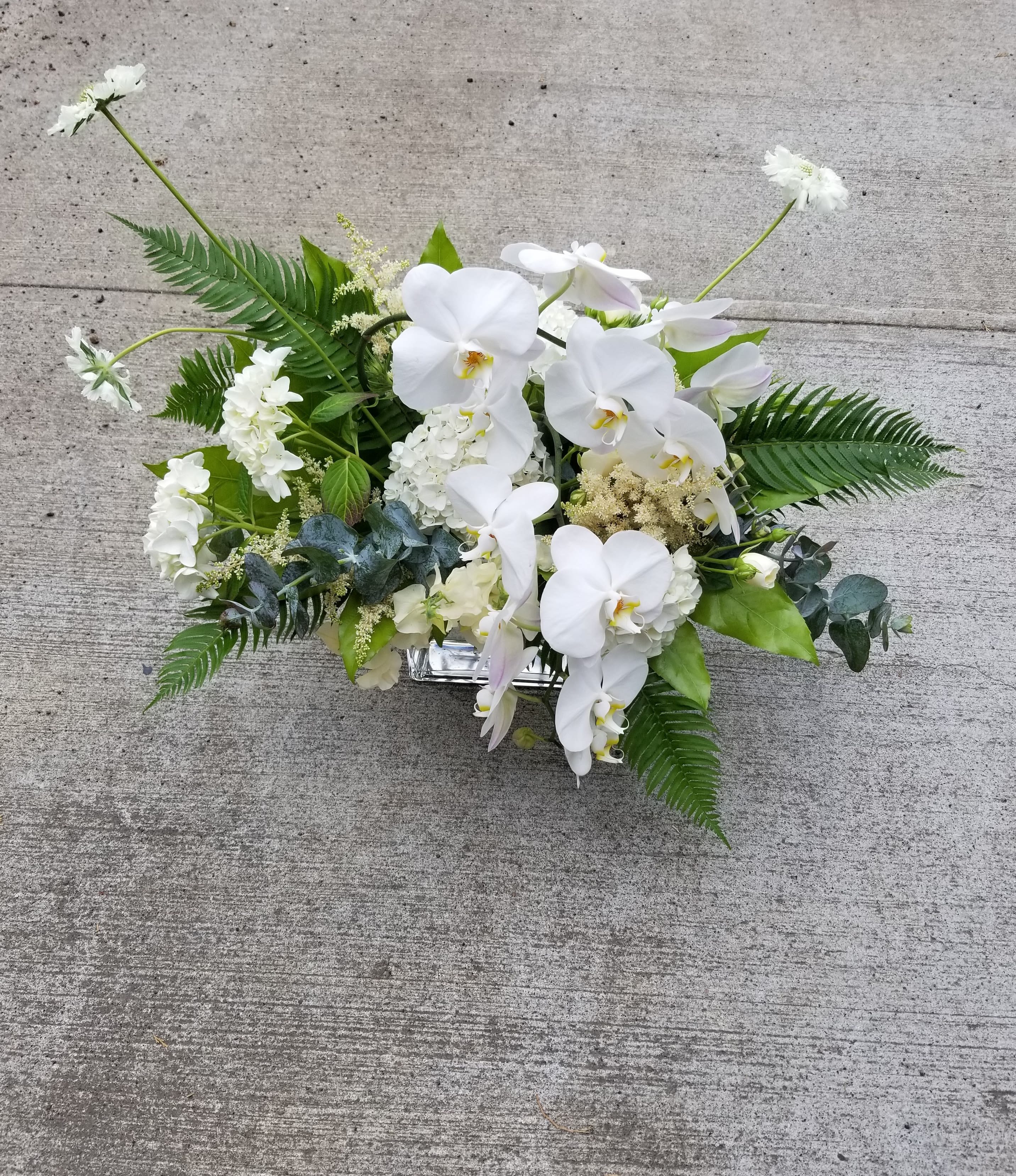 Low arrangement of white orchids and white flowers in a rectangular silver container