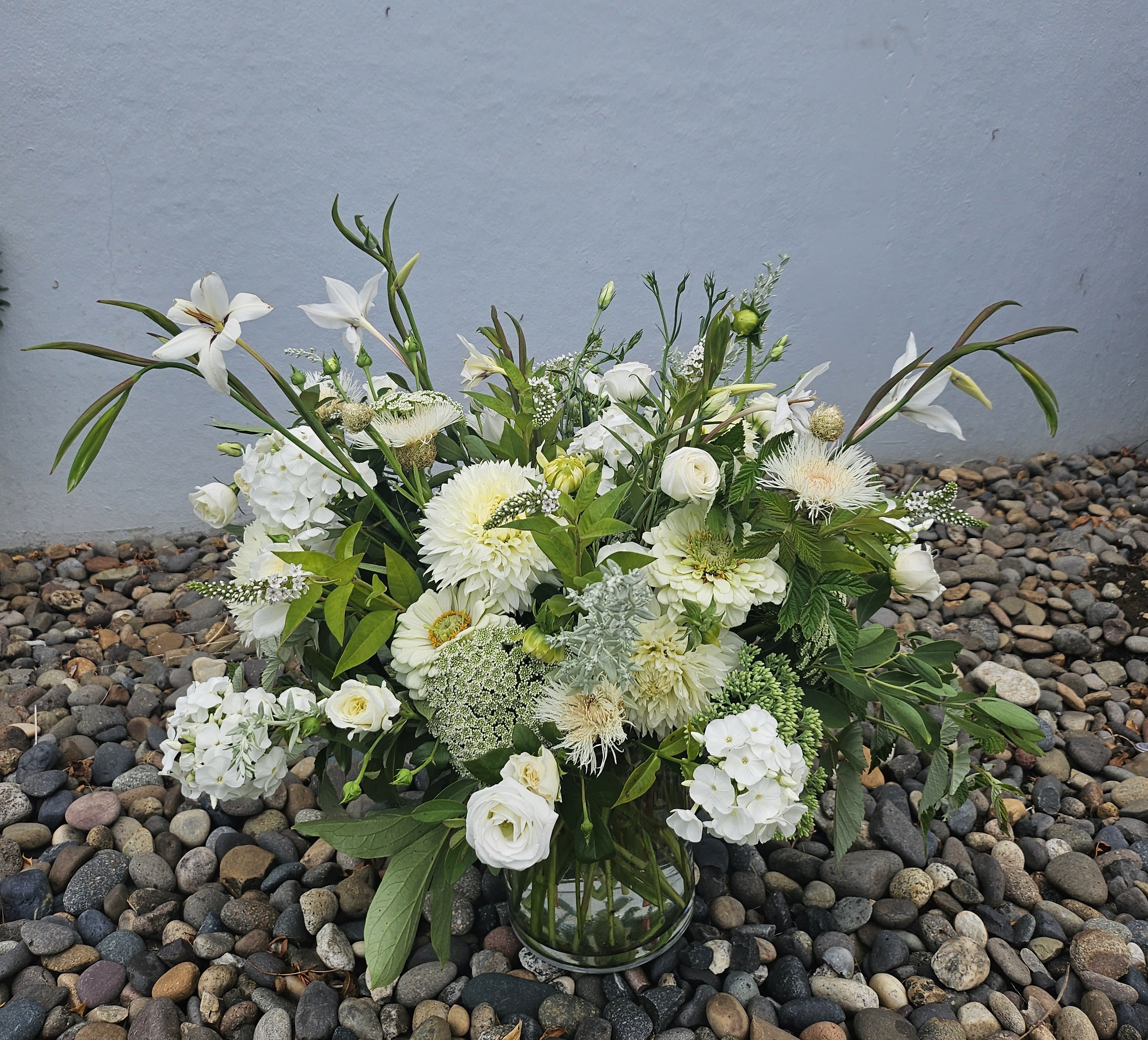 Clear glass vase filled with lush white and cream flowers and abundant leafy accents