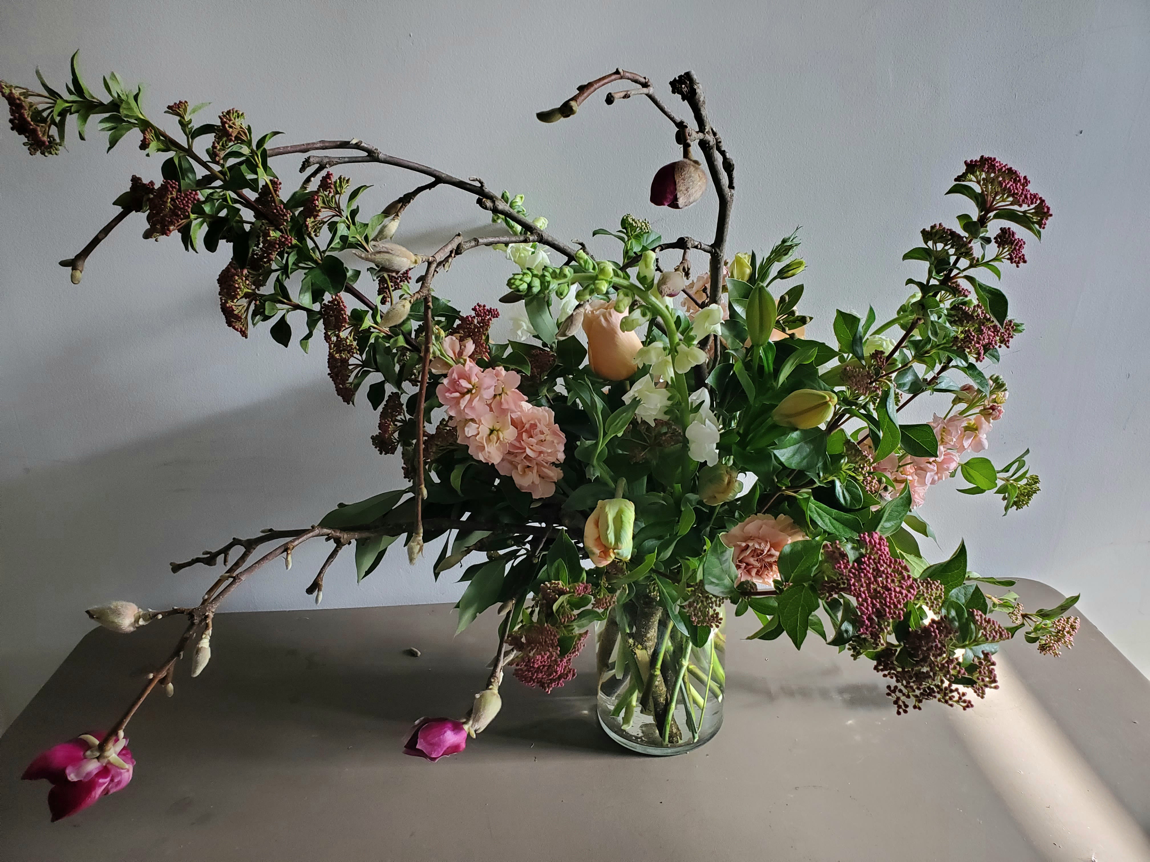 Asymmetrical arrangement of pink and peach flowers with branches in a clear glass vase