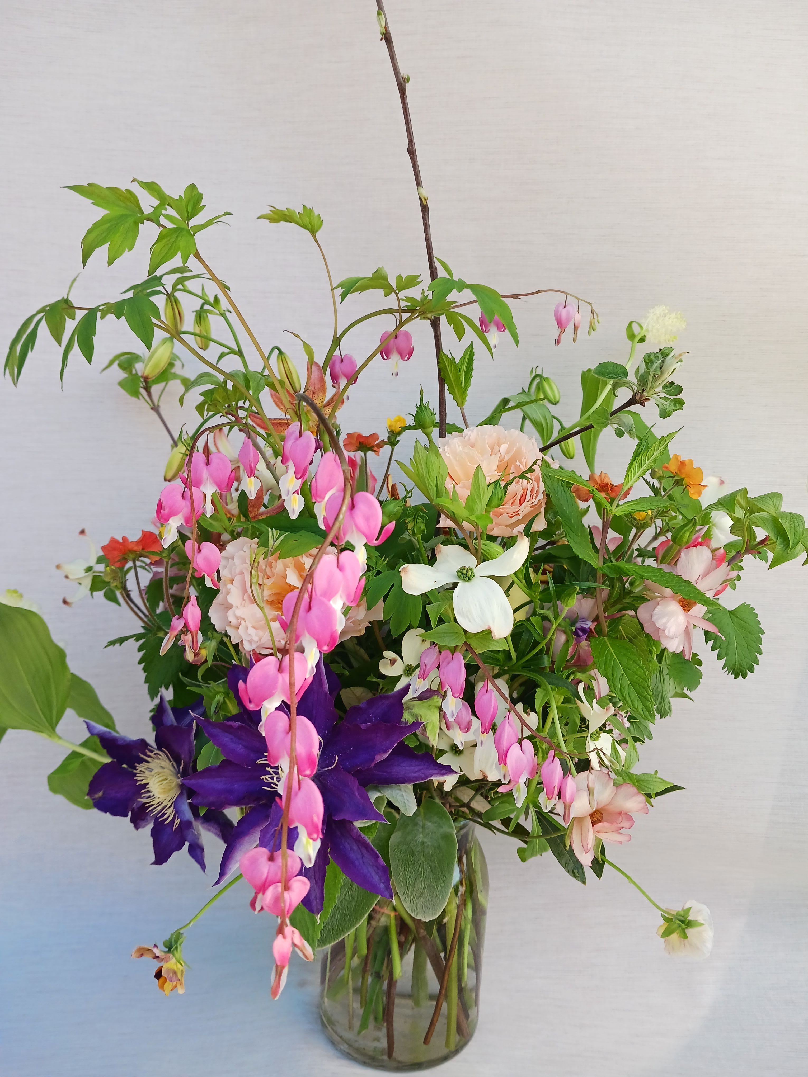 Loose garden-style bouquet of pink, purple, and peach flowers in a clear glass vase