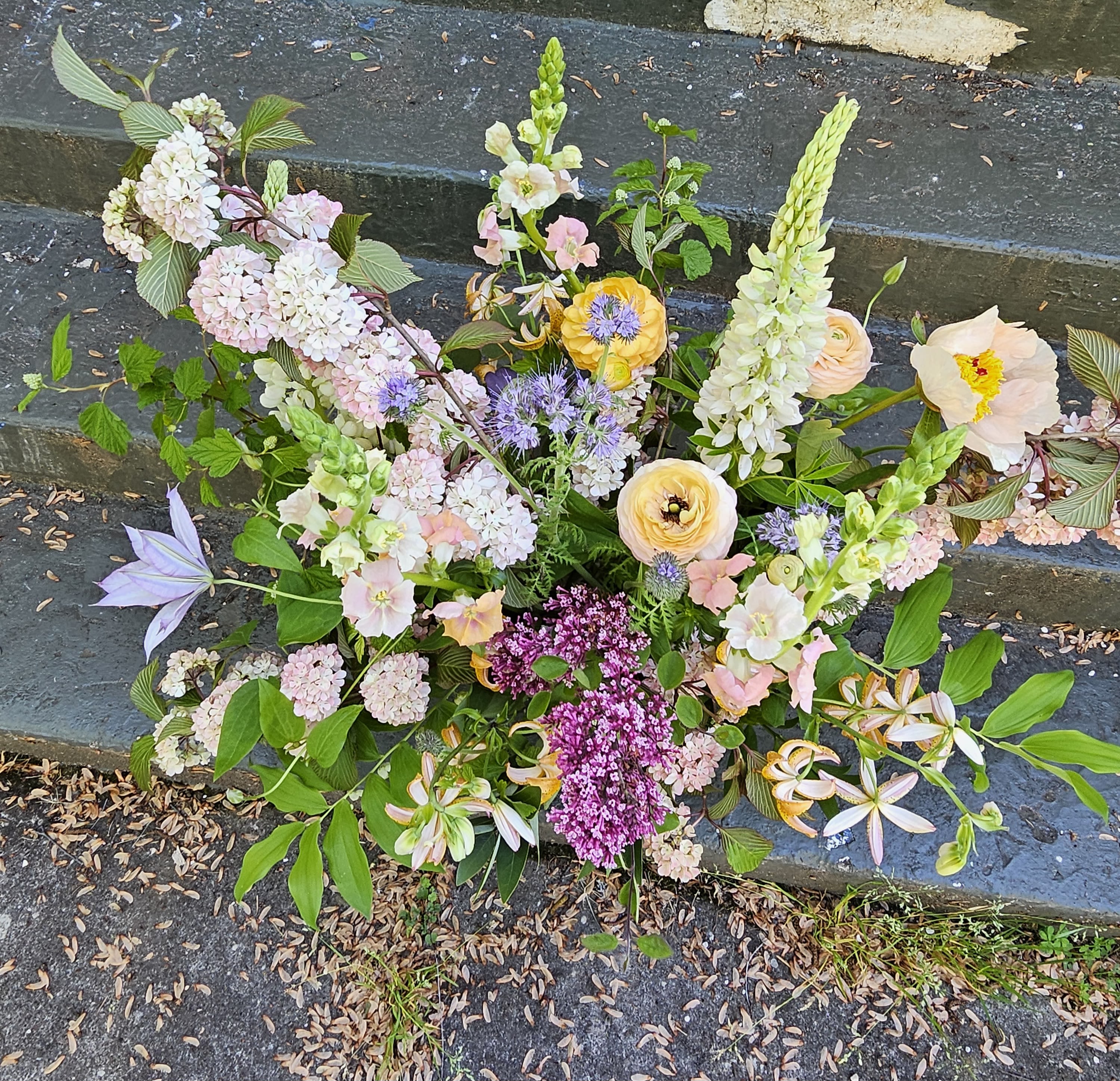 Loose garden-style arrangement of pastel flowers with purple accents displayed on outdoor stone steps