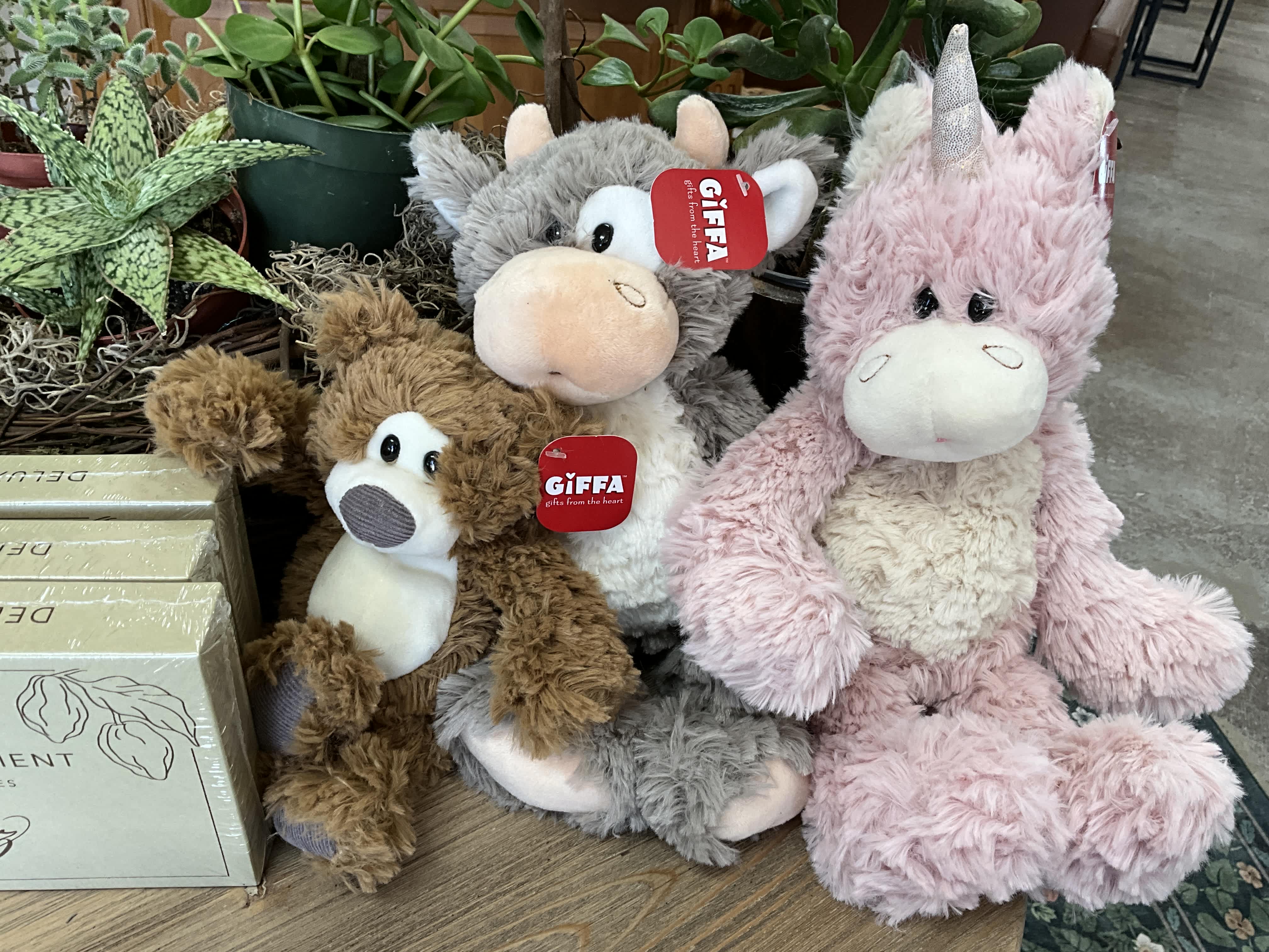 Three plush unicorn toys sit beside potted plants.