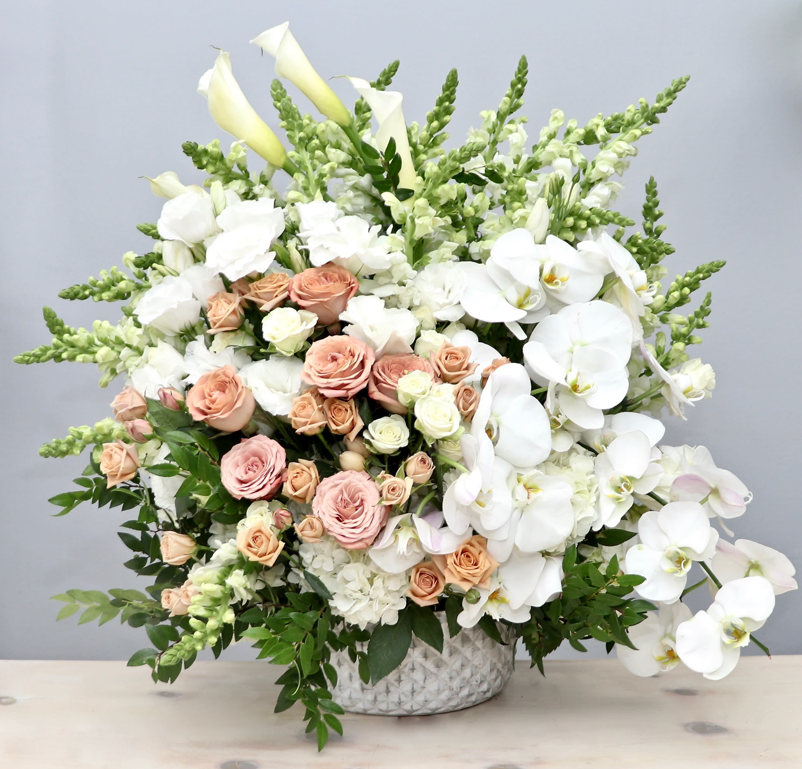 Large arrangement of white orchids, calla lilies, and peach and cream roses in a white vase