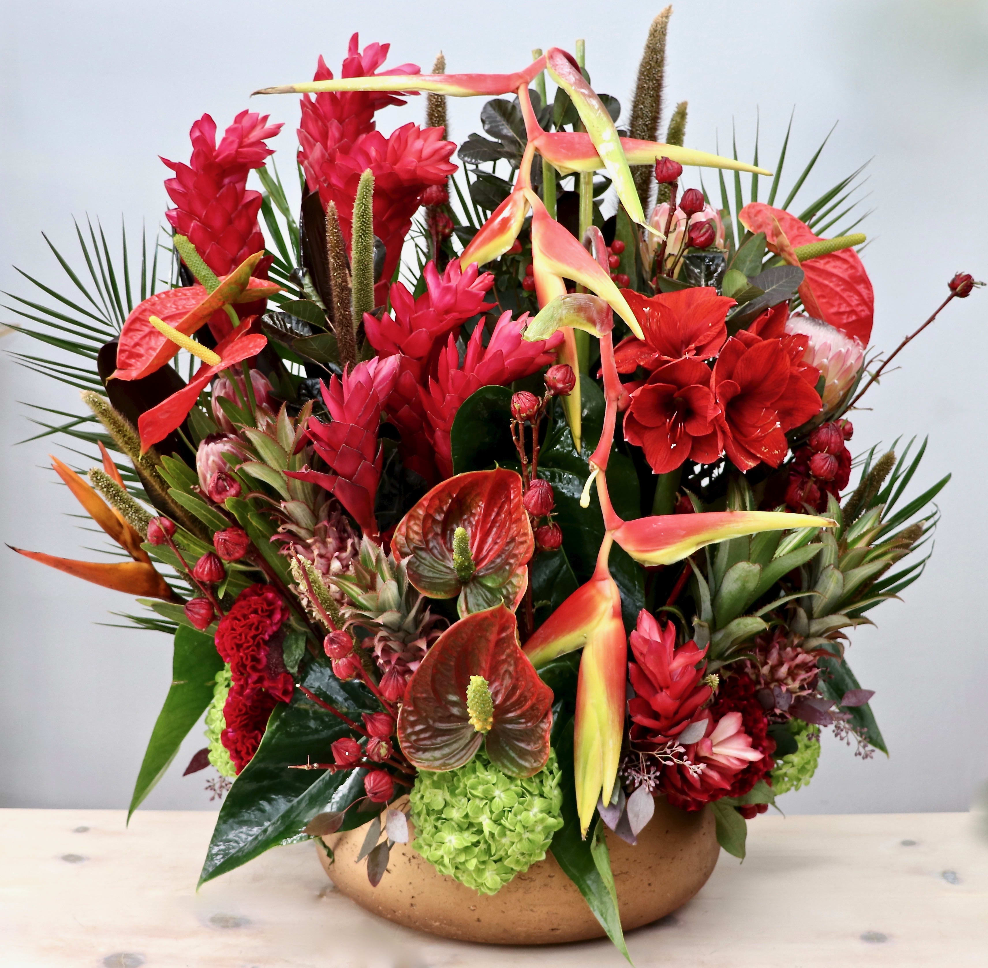 Large tropical arrangement of red and green flowers in a low gold bowl