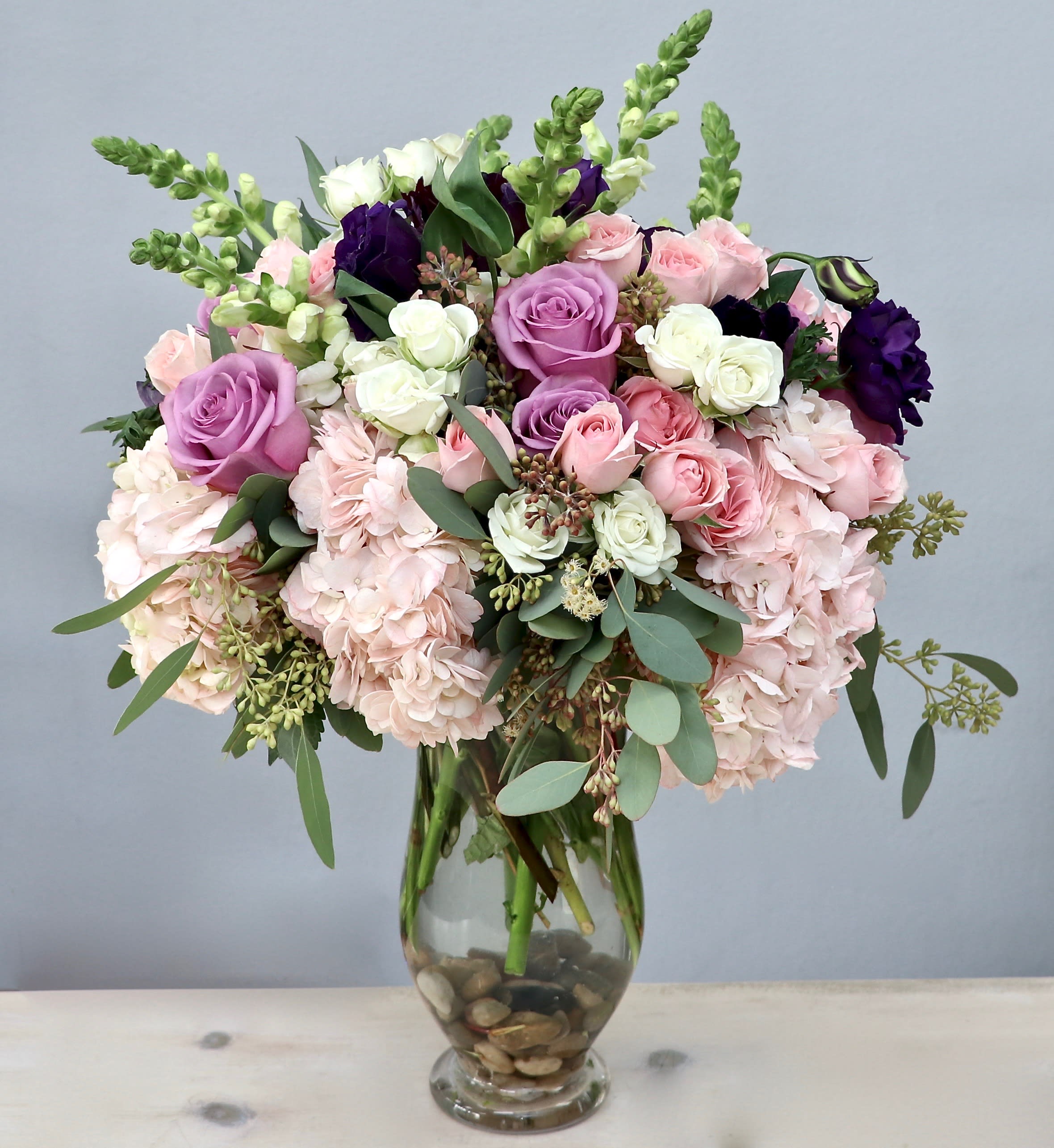 Tall glass vase arrangement with pink hydrangeas, roses, and white and purple accent blooms