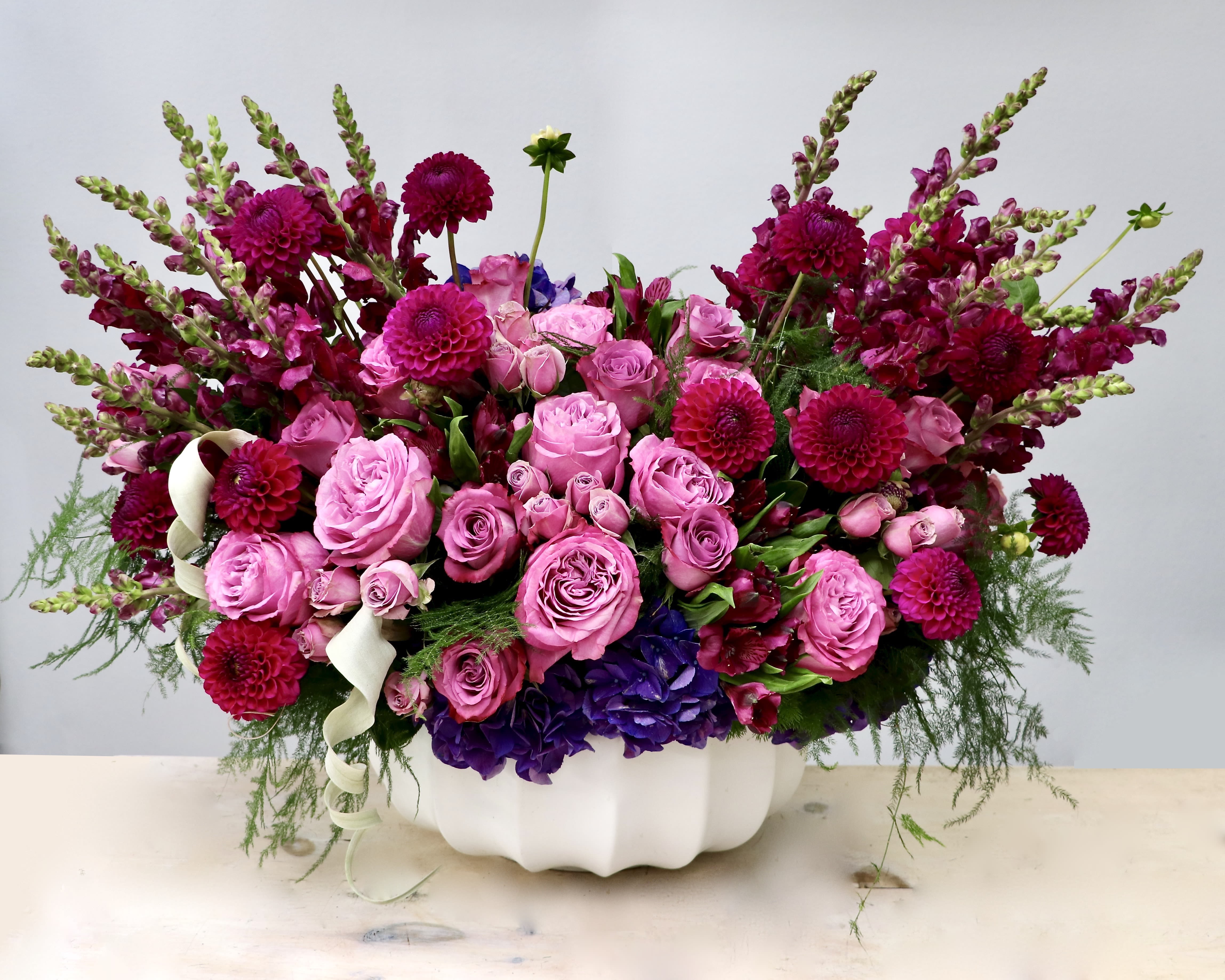 Low pink and magenta arrangement of roses, dahlias, and snapdragons in a white ceramic bowl