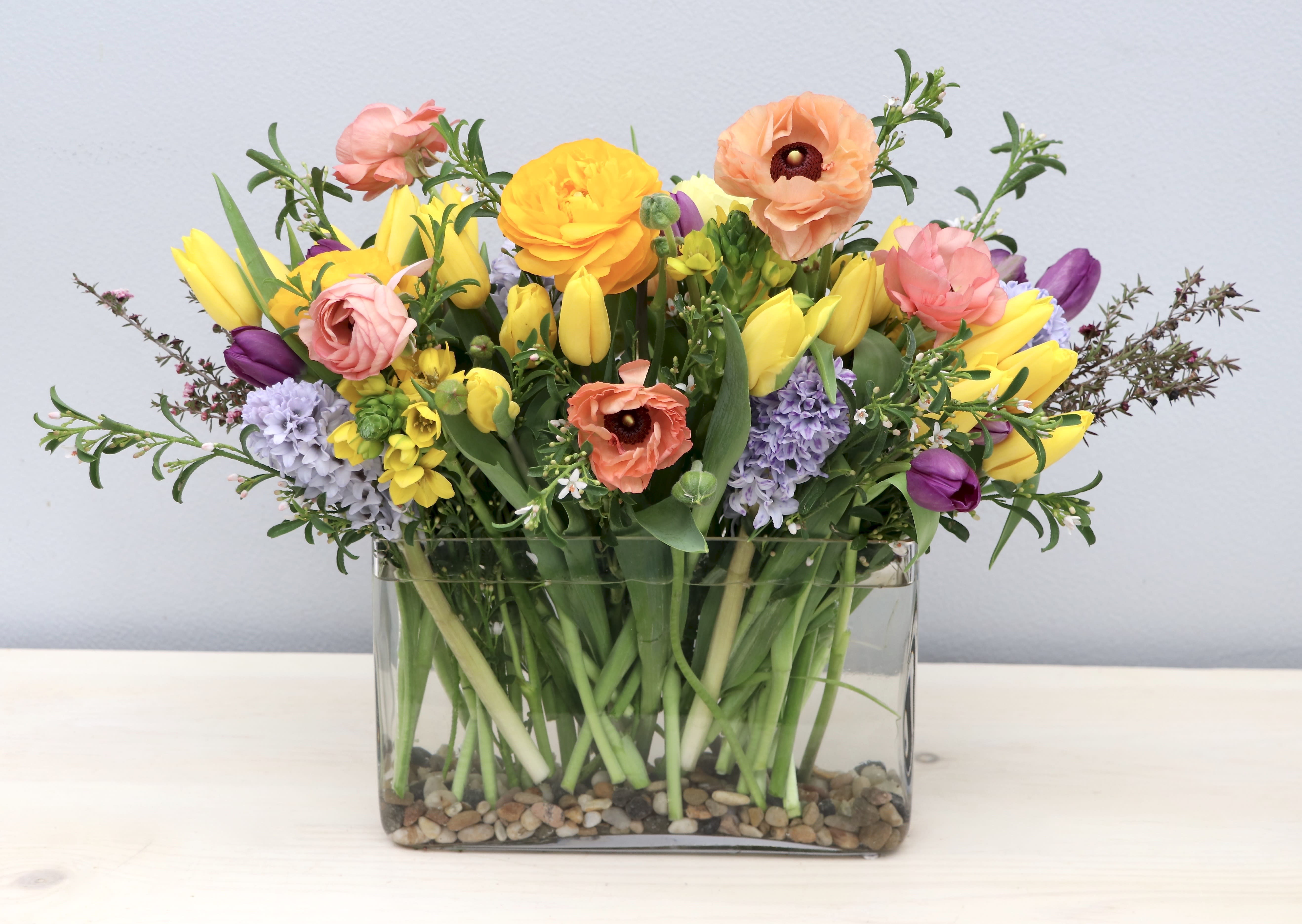 Colorful spring flower arrangement in a rectangular glass vase with river rocks