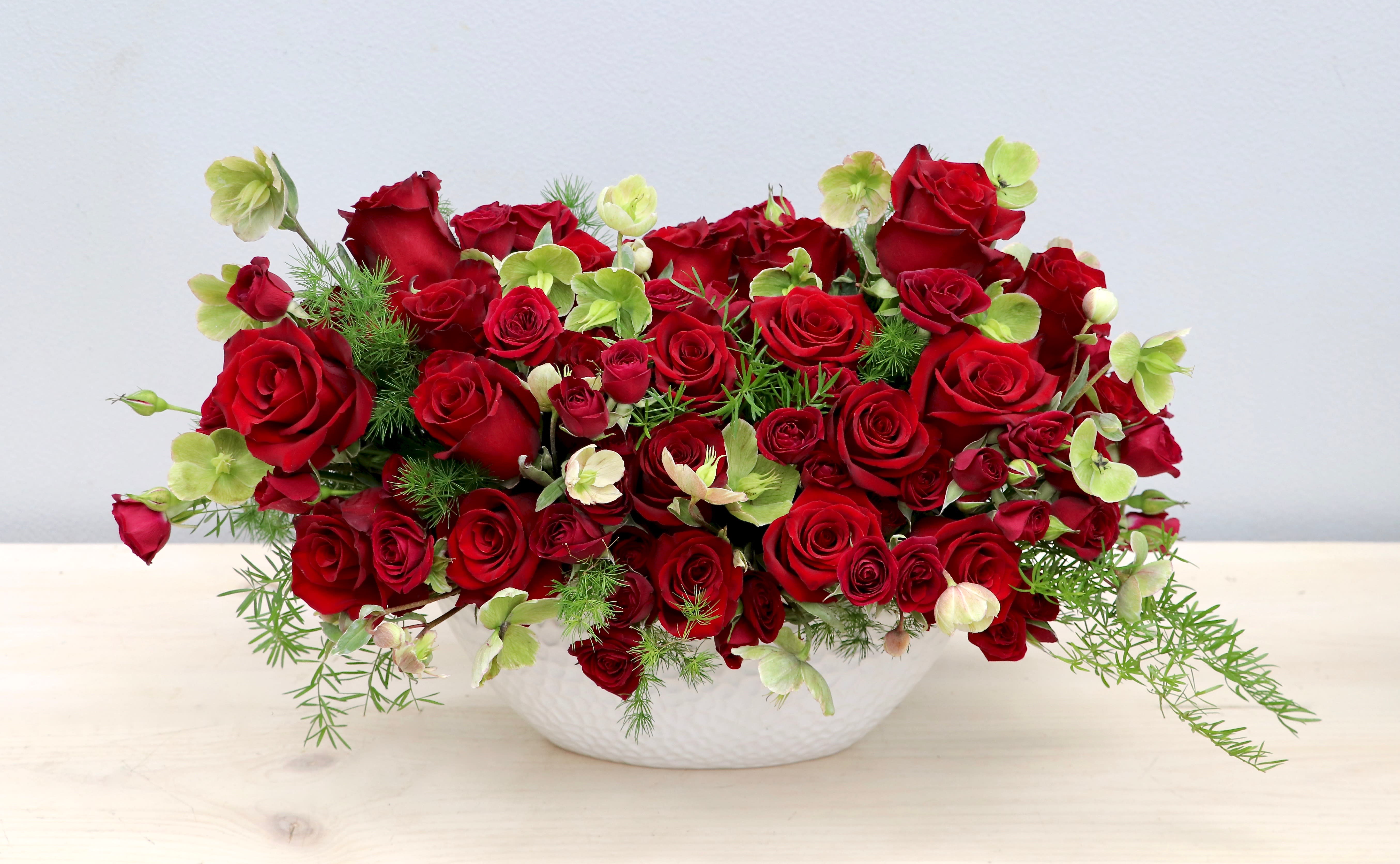 Low oval arrangement of red roses and green blooms in a white bowl.
