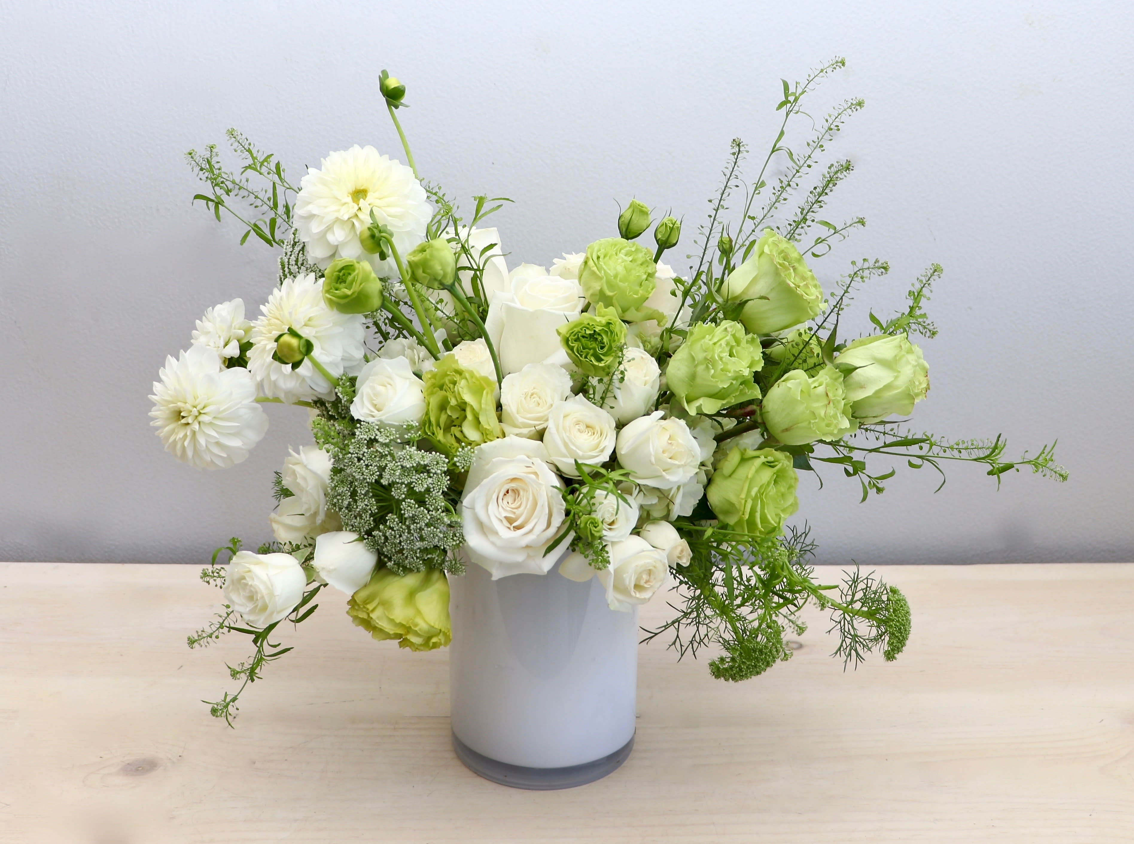 Asymmetrical white and green flower arrangement in a white cylinder vase