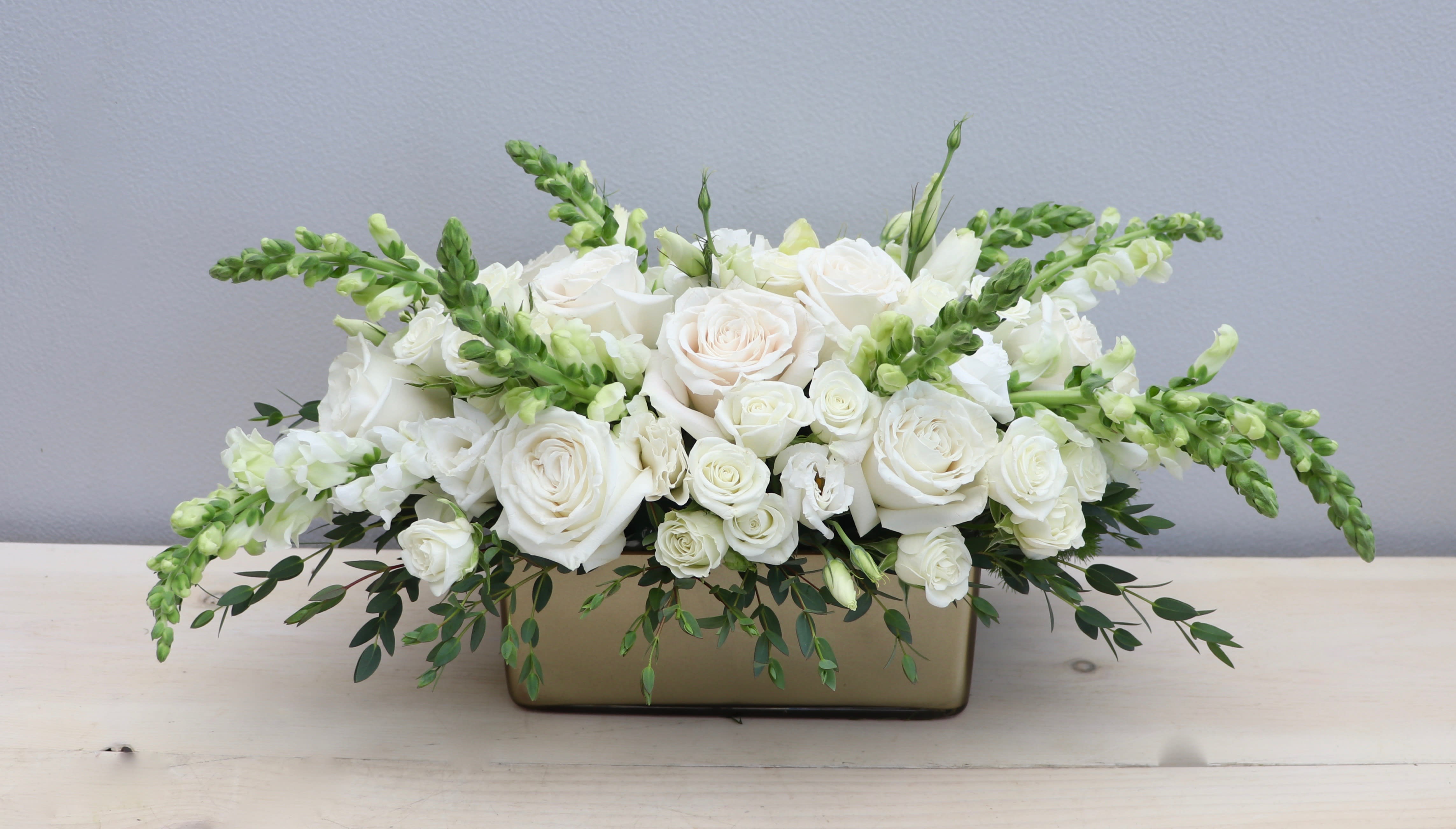 Low white rose and snapdragon arrangement in a rectangular gold vase