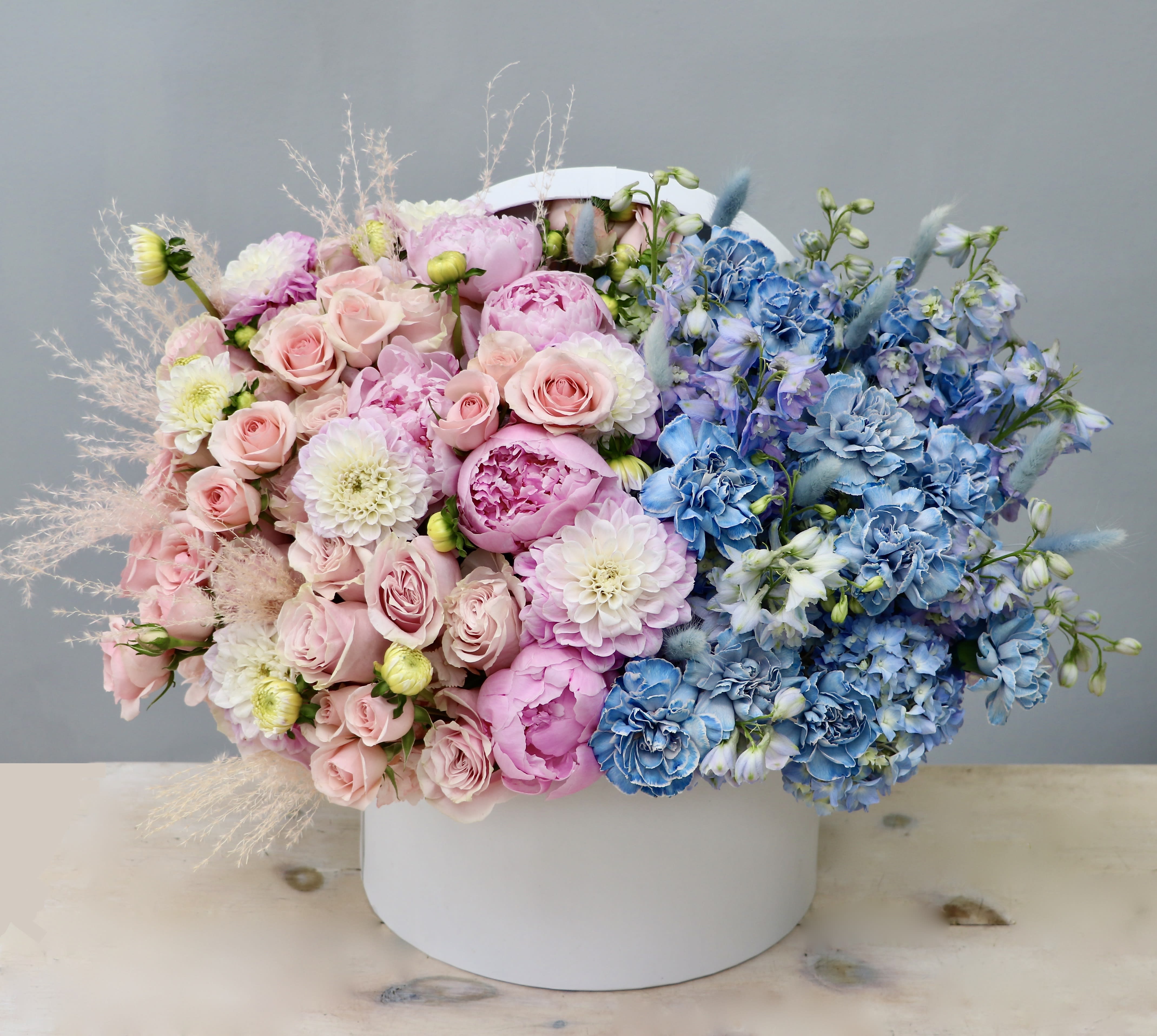 Large hatbox arrangement of pink roses and peonies with blue and white blooms in a split-color design