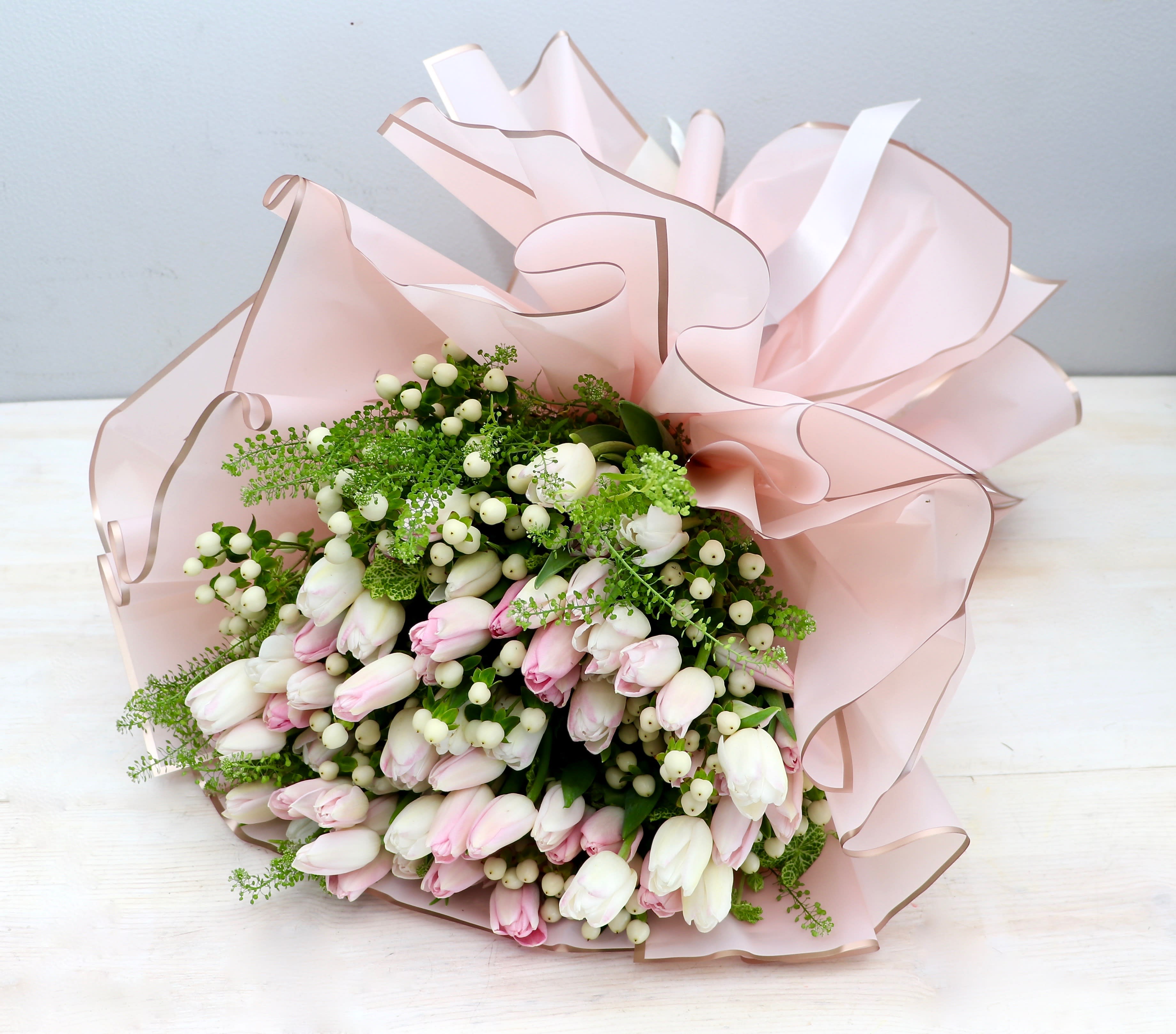 Hand-tied bouquet of white and pale pink tulips with white berries wrapped in ruffled blush paper
