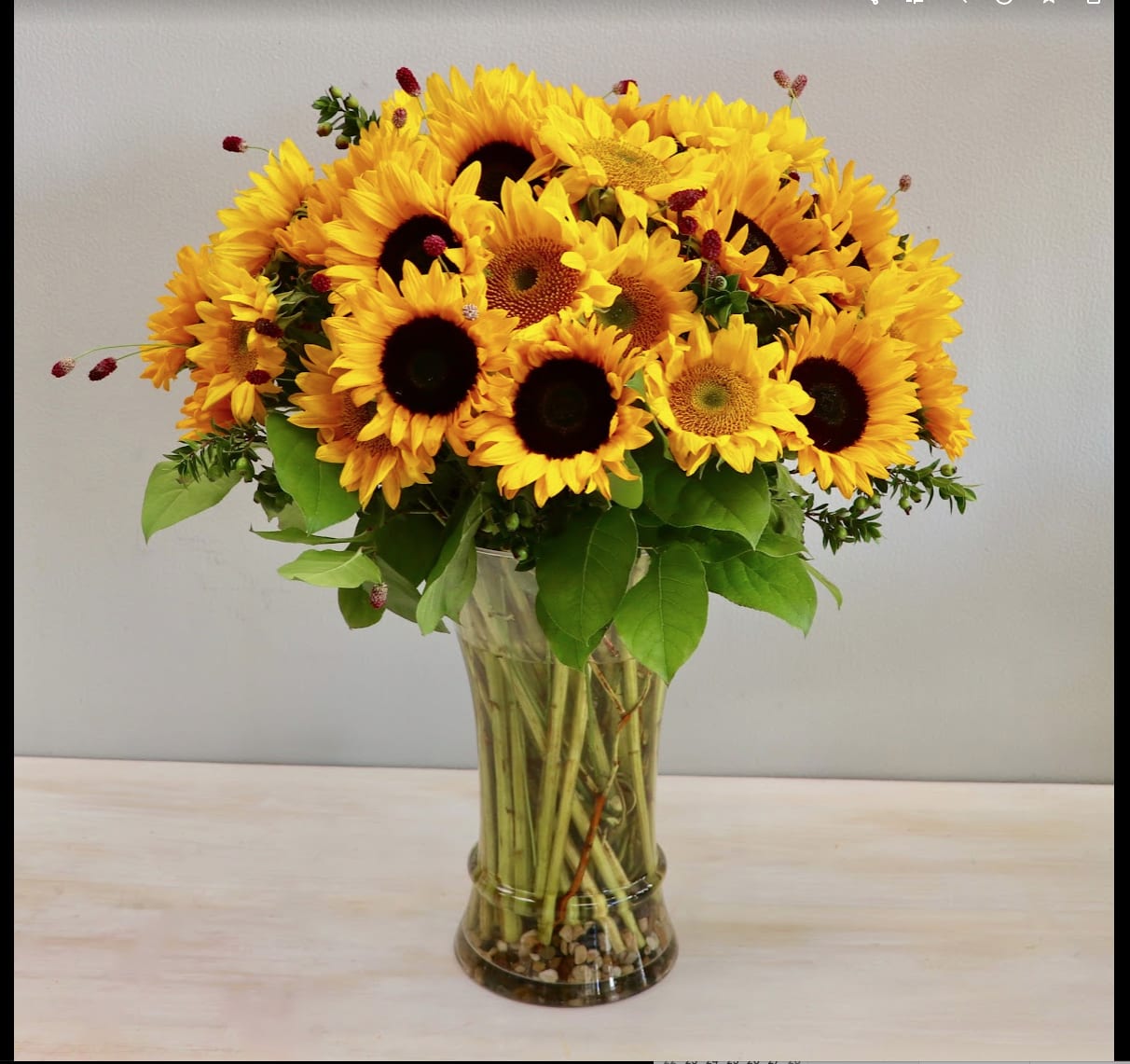 Tall bouquet of yellow sunflowers in a clear glass vase with visible stems