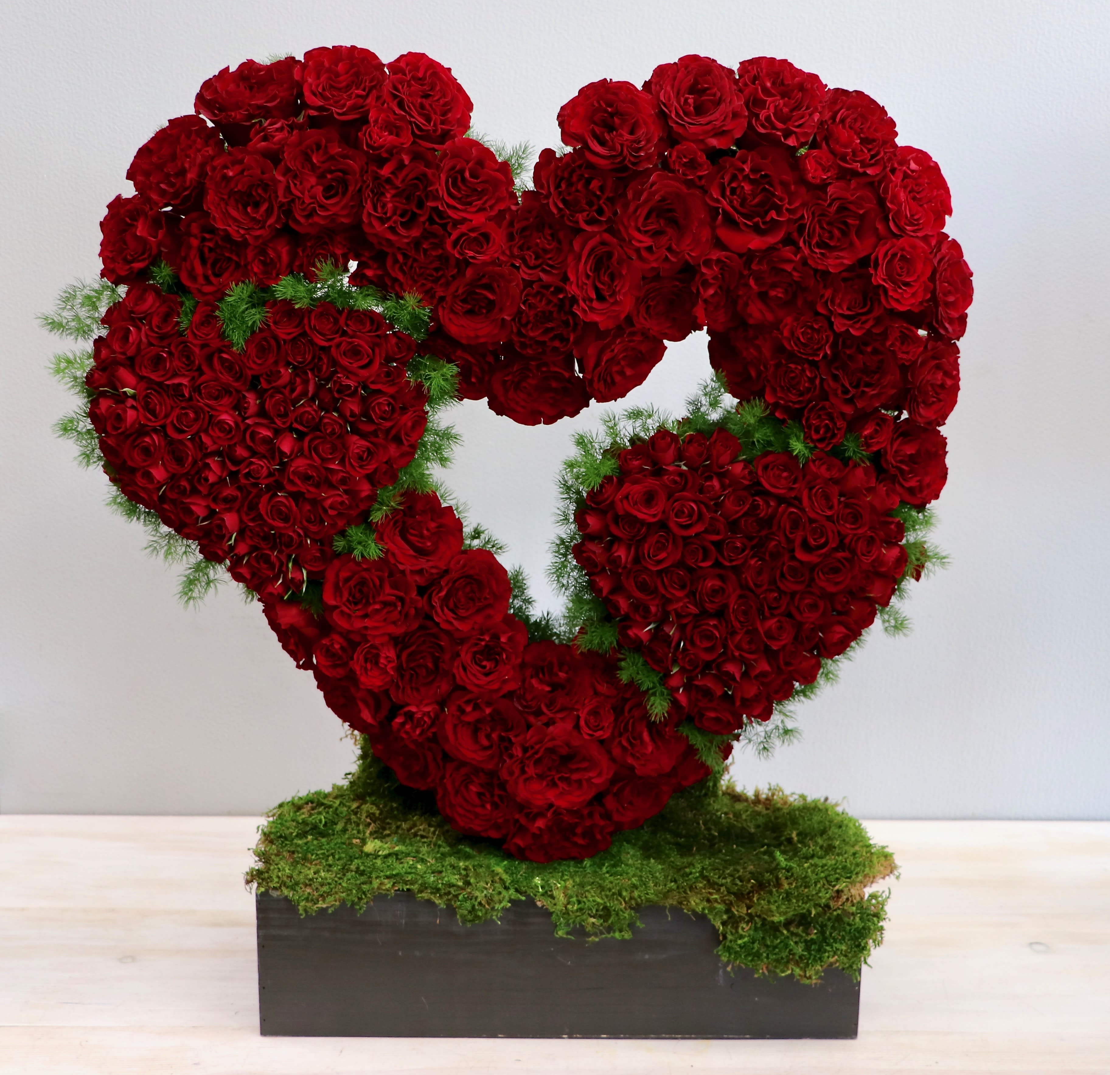 Sculpted open heart of red roses with smaller rose hearts on a moss-covered rectangular base.