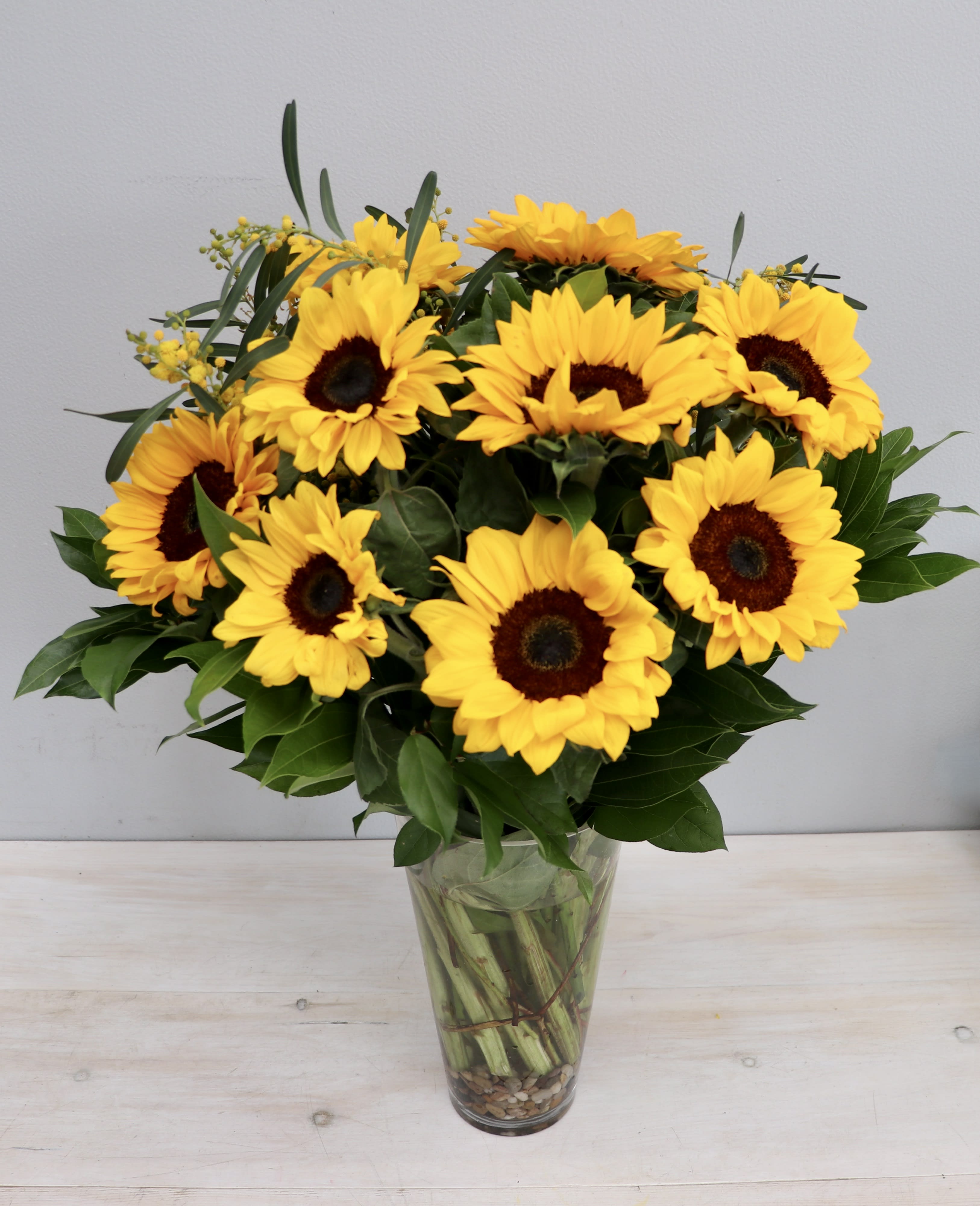Tall glass vase of bright yellow sunflowers with dark centers arranged in a full bouquet