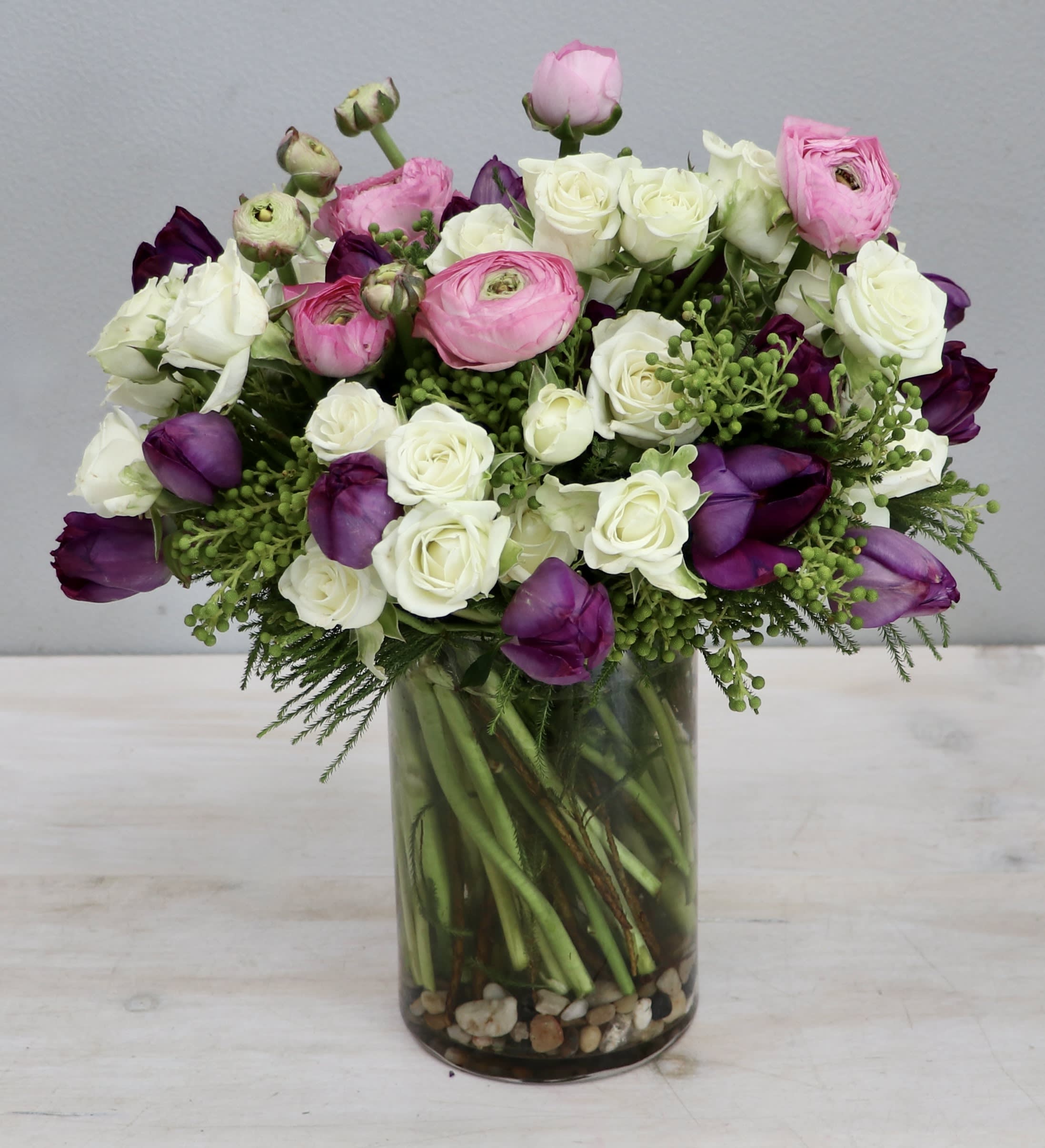 White roses with pink ranunculus and purple blooms in a clear glass vase