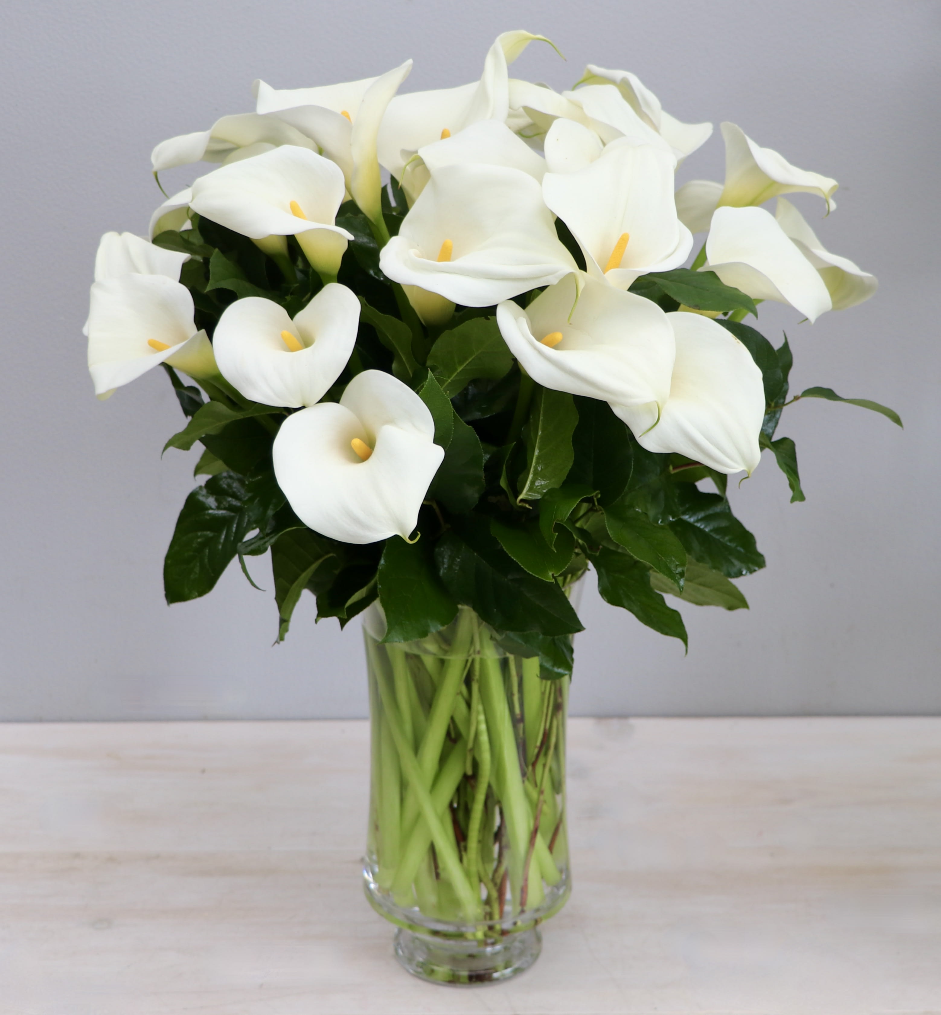 Tall arrangement of white calla lilies in a clear glass vase