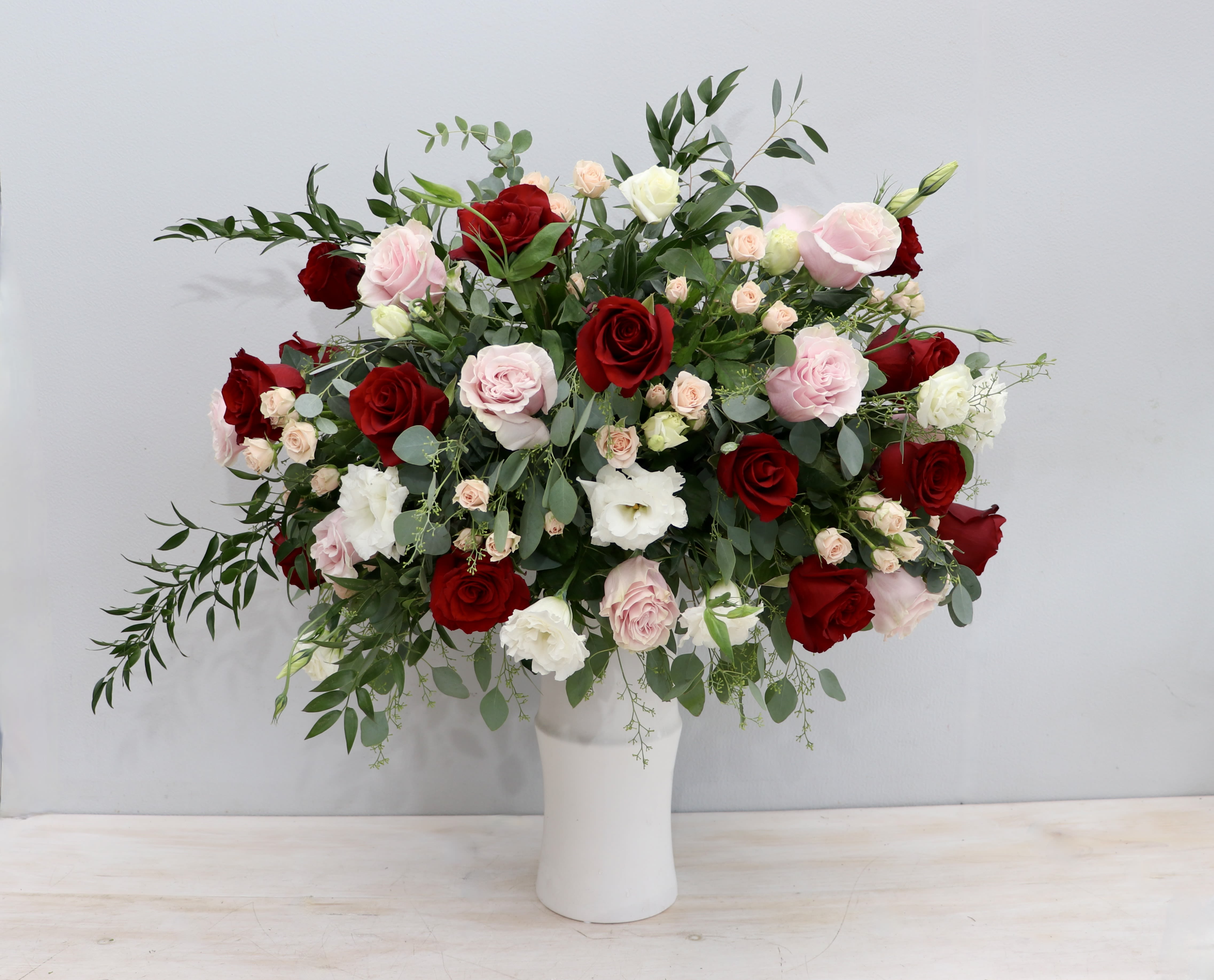 Tall vase of red, pink, and white roses with filler blooms in a lush, wide arrangement