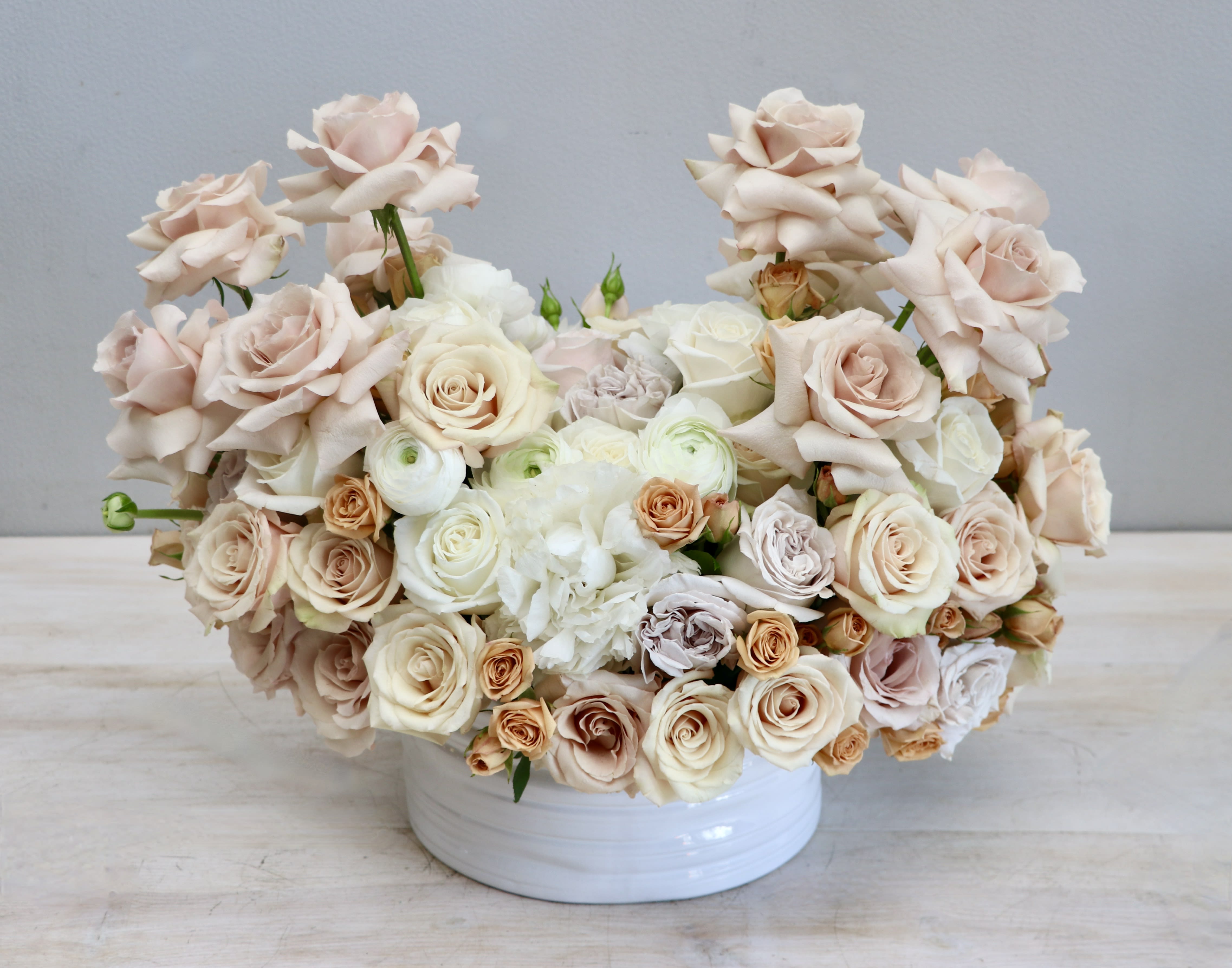 Low arrangement of cream and blush roses with white blooms in a round white ceramic bowl