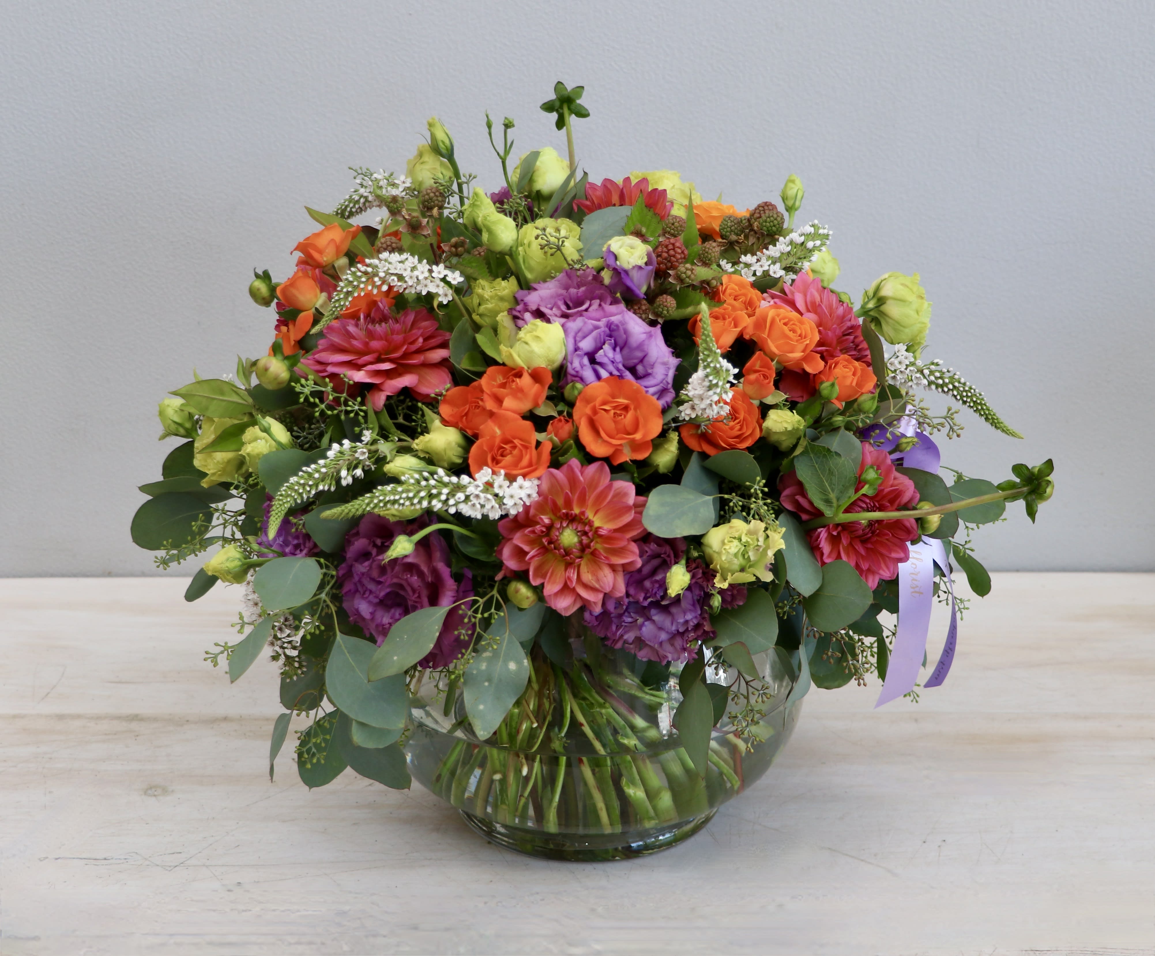 Low round arrangement of orange and purple flowers in a clear glass bowl vase