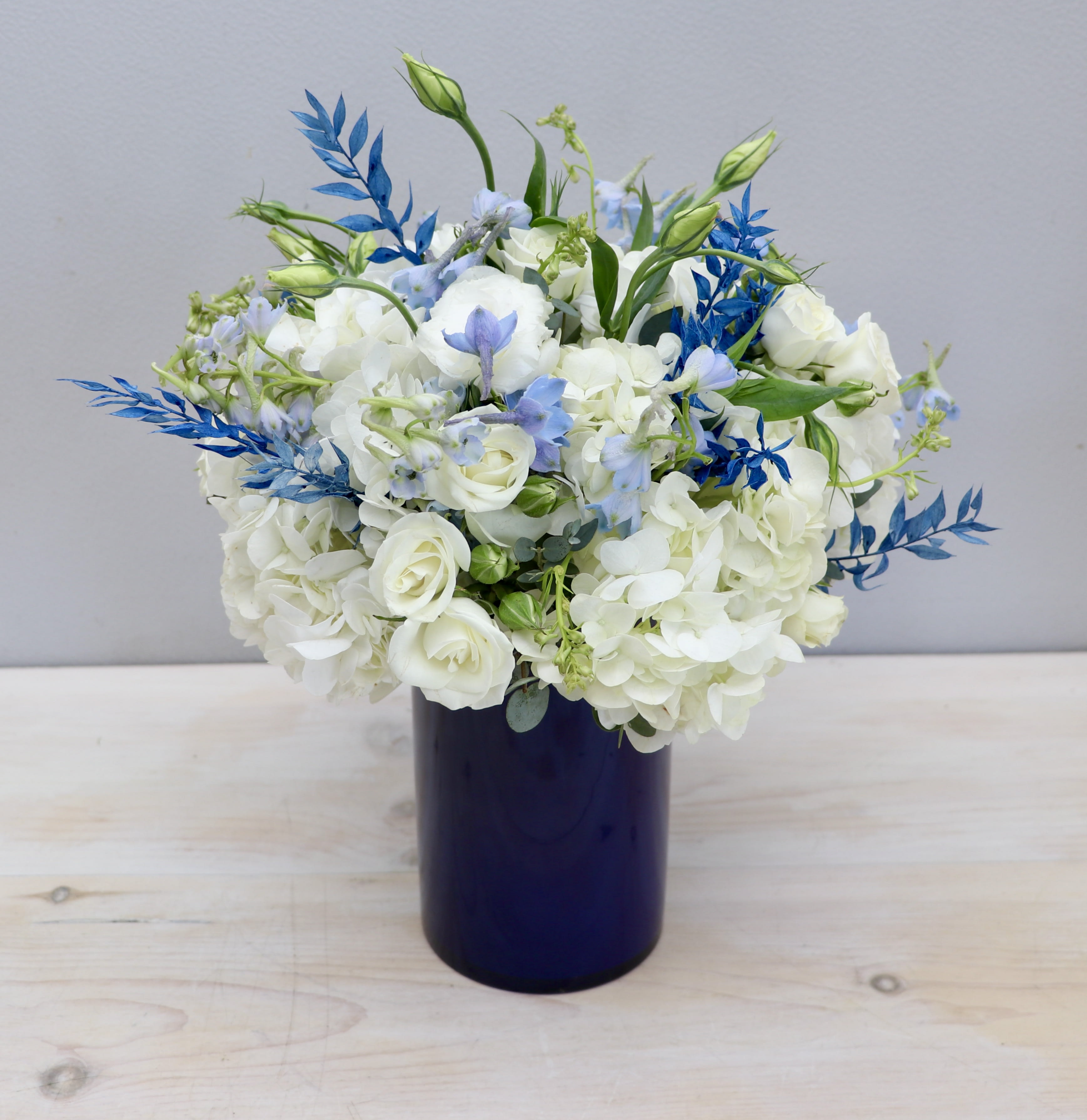 White and light blue flower arrangement in a dark blue cylinder vase