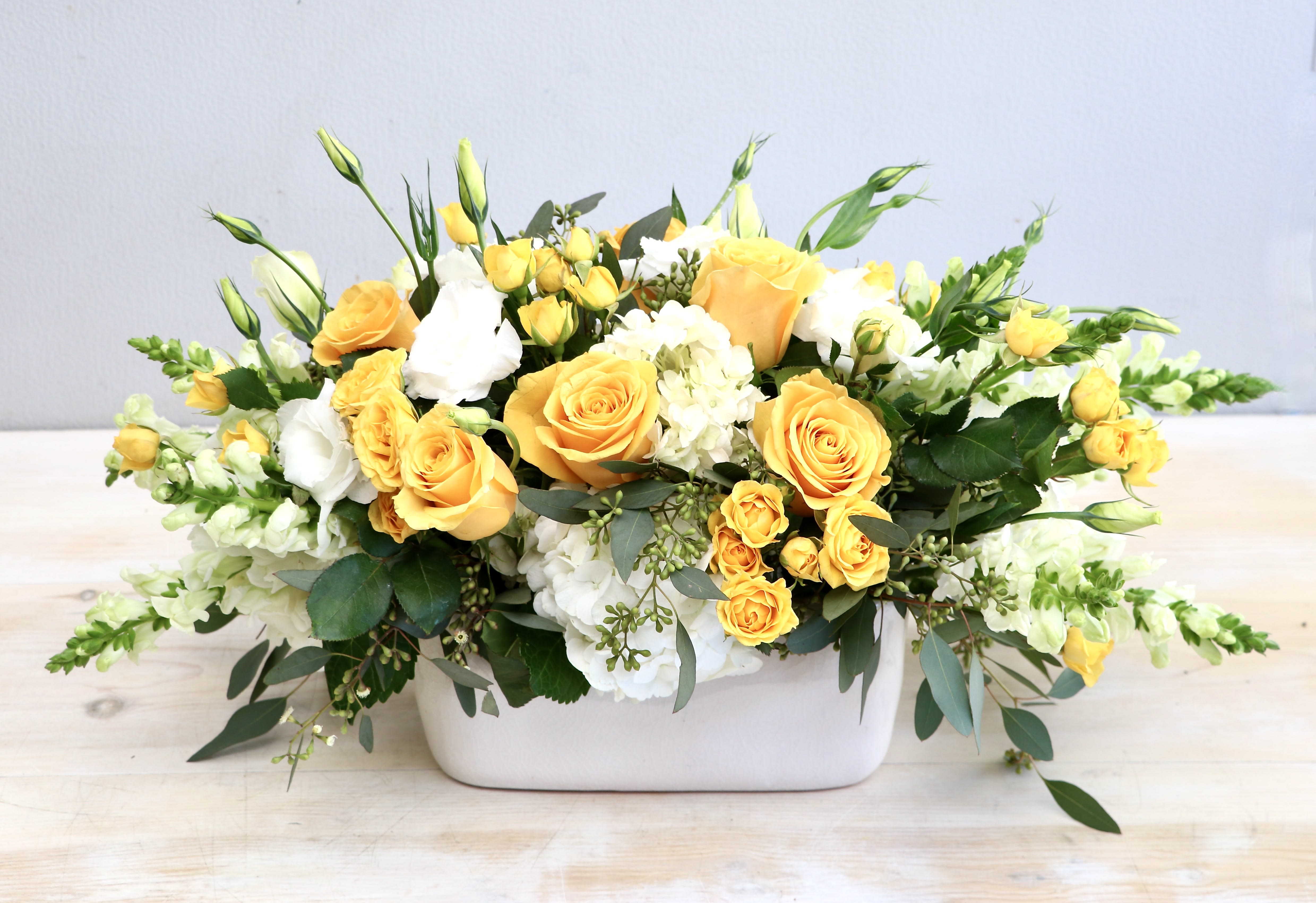 Low arrangement of yellow roses and white flowers in a rectangular white container