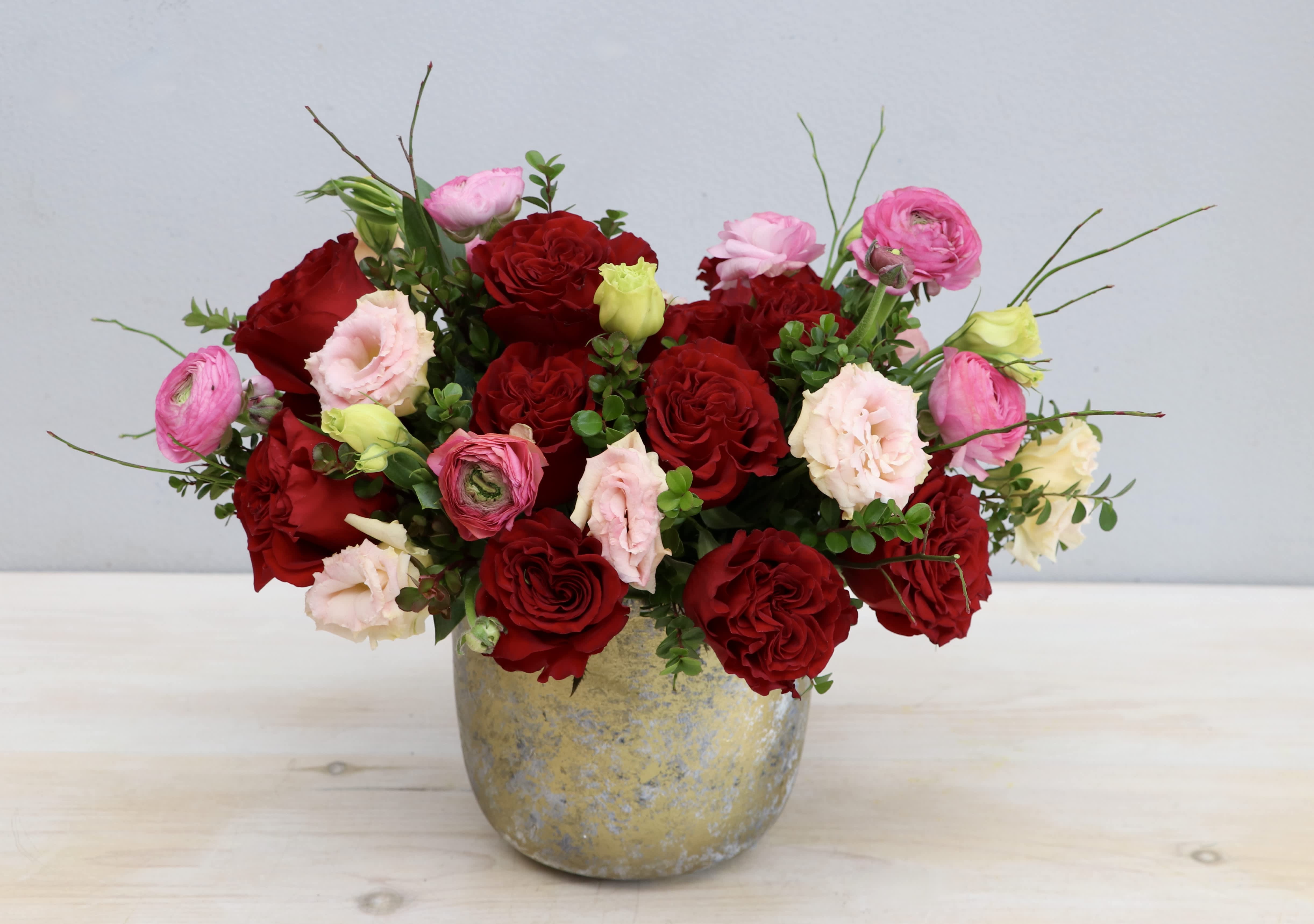 Low arrangement of red roses and pink blooms in a rustic gold-toned pot