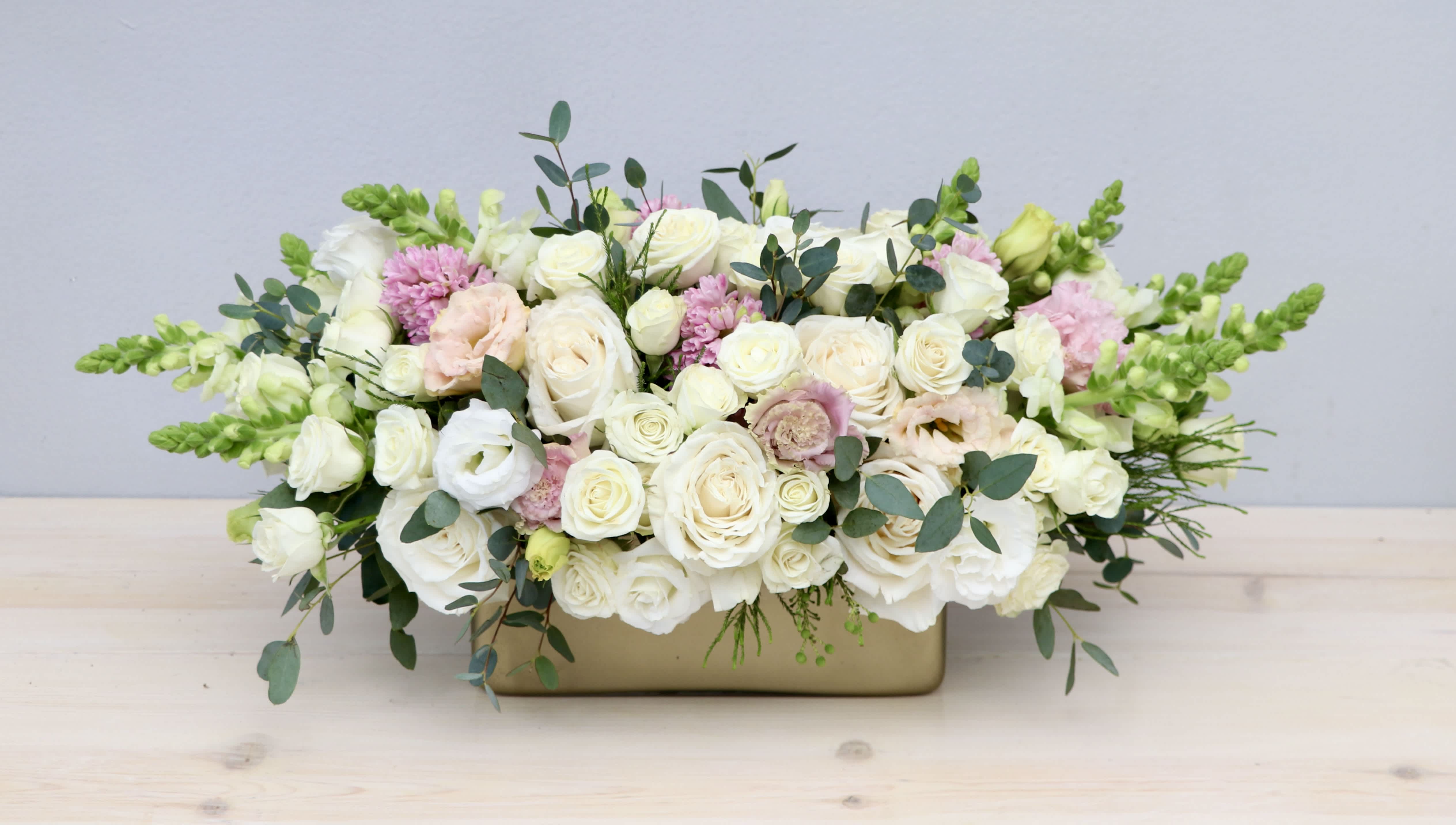Low centerpiece of ivory roses and blush flowers in a wide gold container